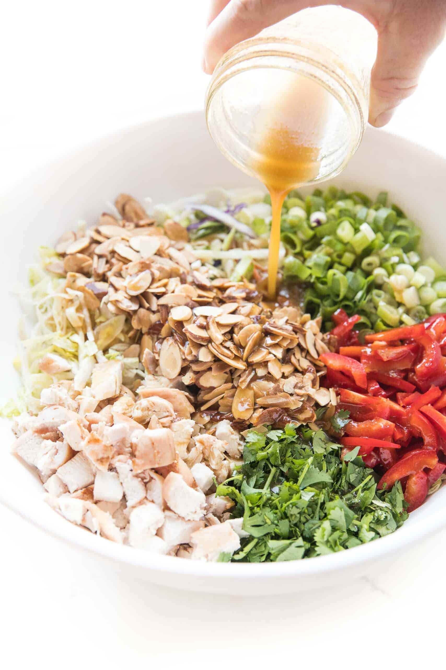homemade asian dressing being poured over chinese chicken salad in a white bowl