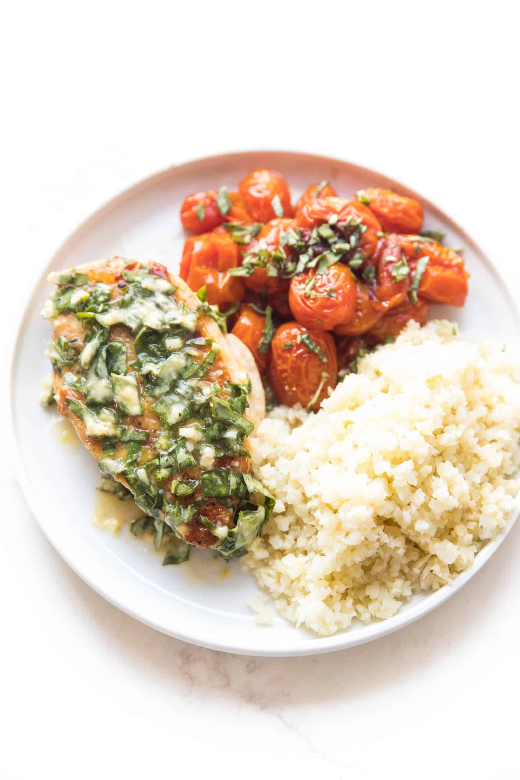 chicken with basil butter, blistered tomatoes and cauliflower rice on a white plate