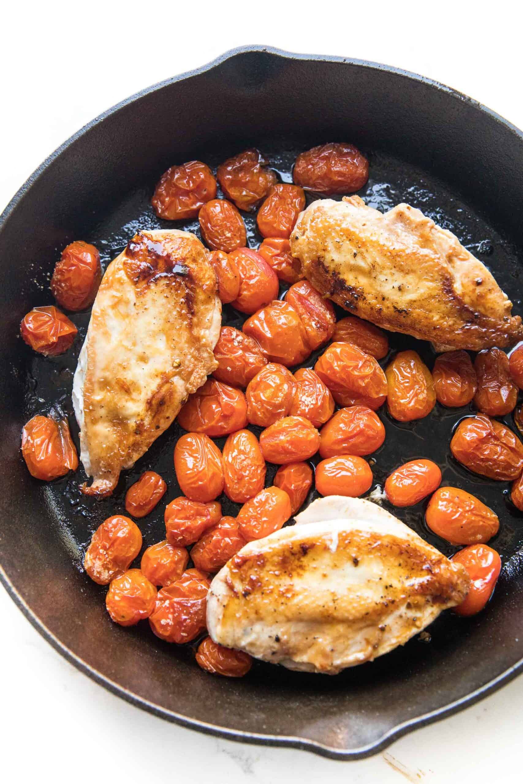 cast iron skillet with chicken and blistered tomatoes