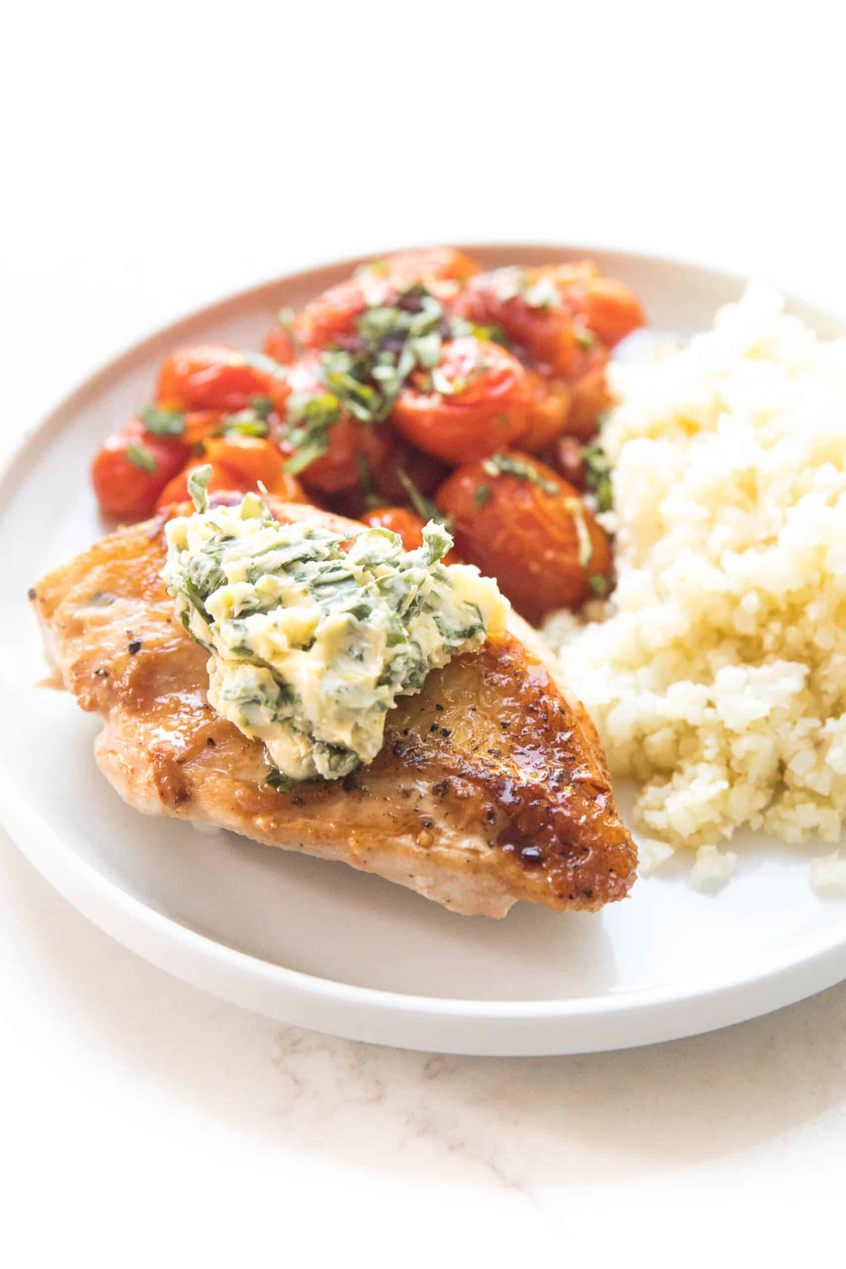 chicken with basil butter, blistered tomatoes and cauliflower rice on a white plate