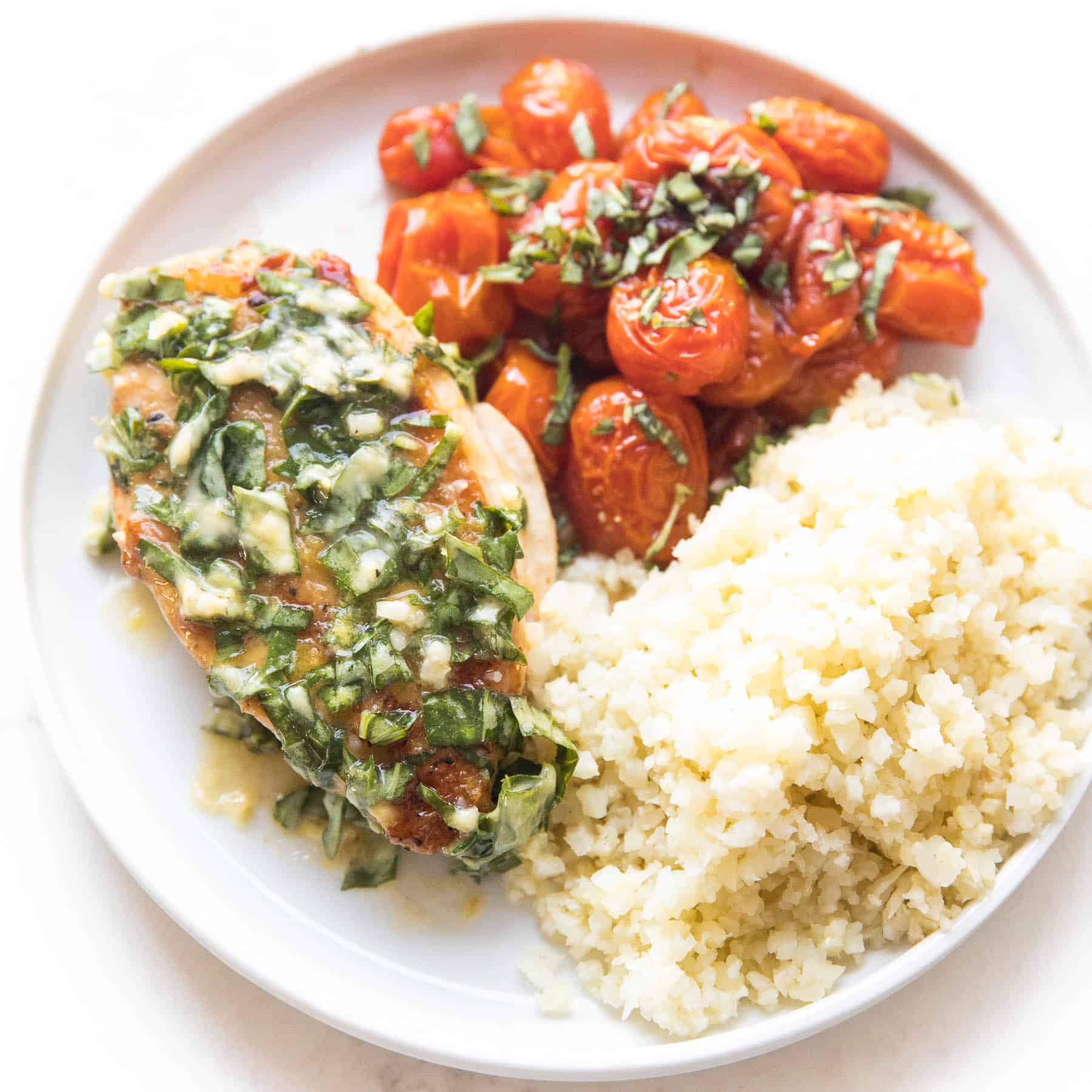 chicken with basil butter, blistered tomatoes and cauliflower rice on a white plate