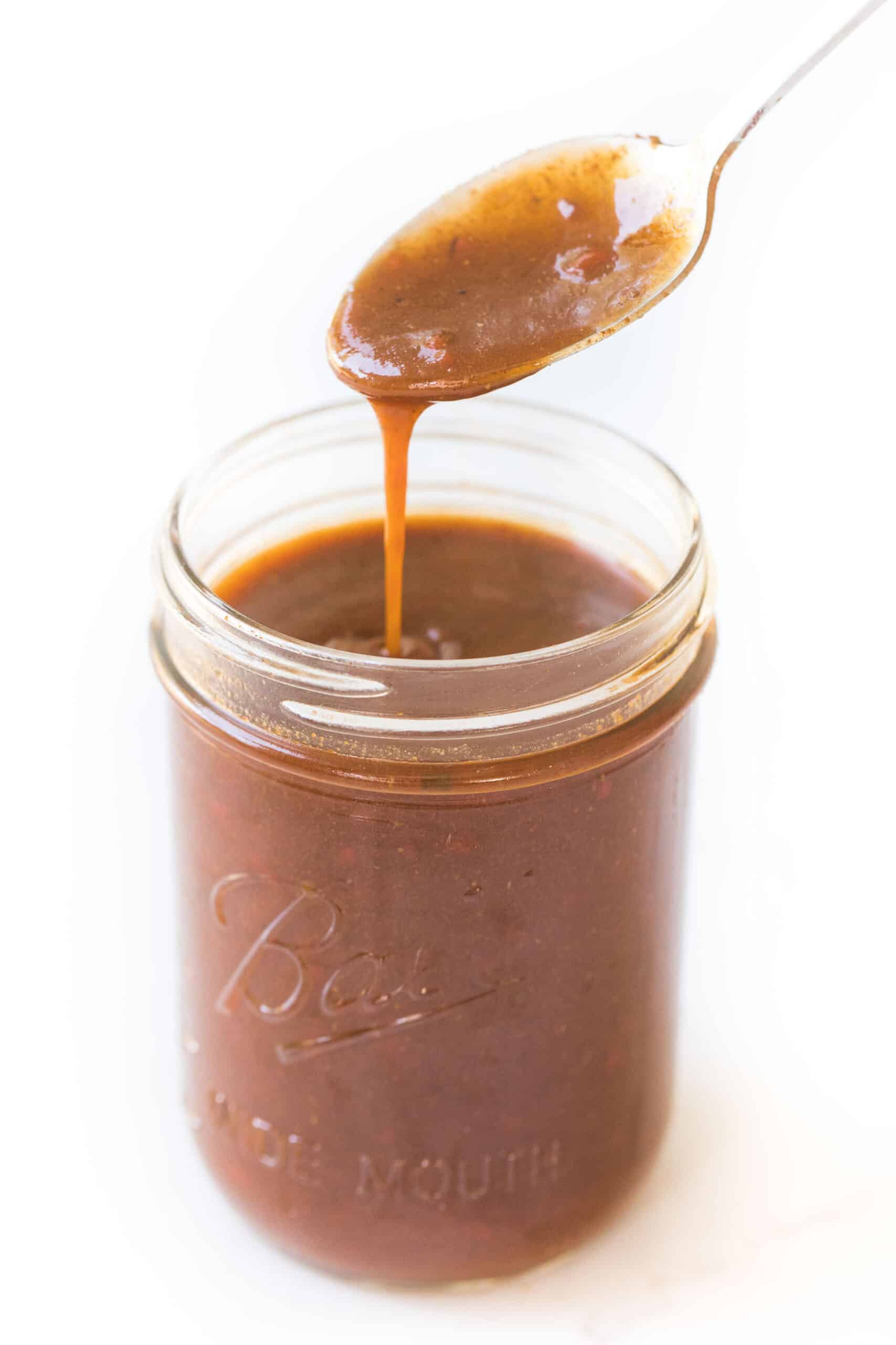spoon in a mason jar of homemade red enchilada sauce on a white background