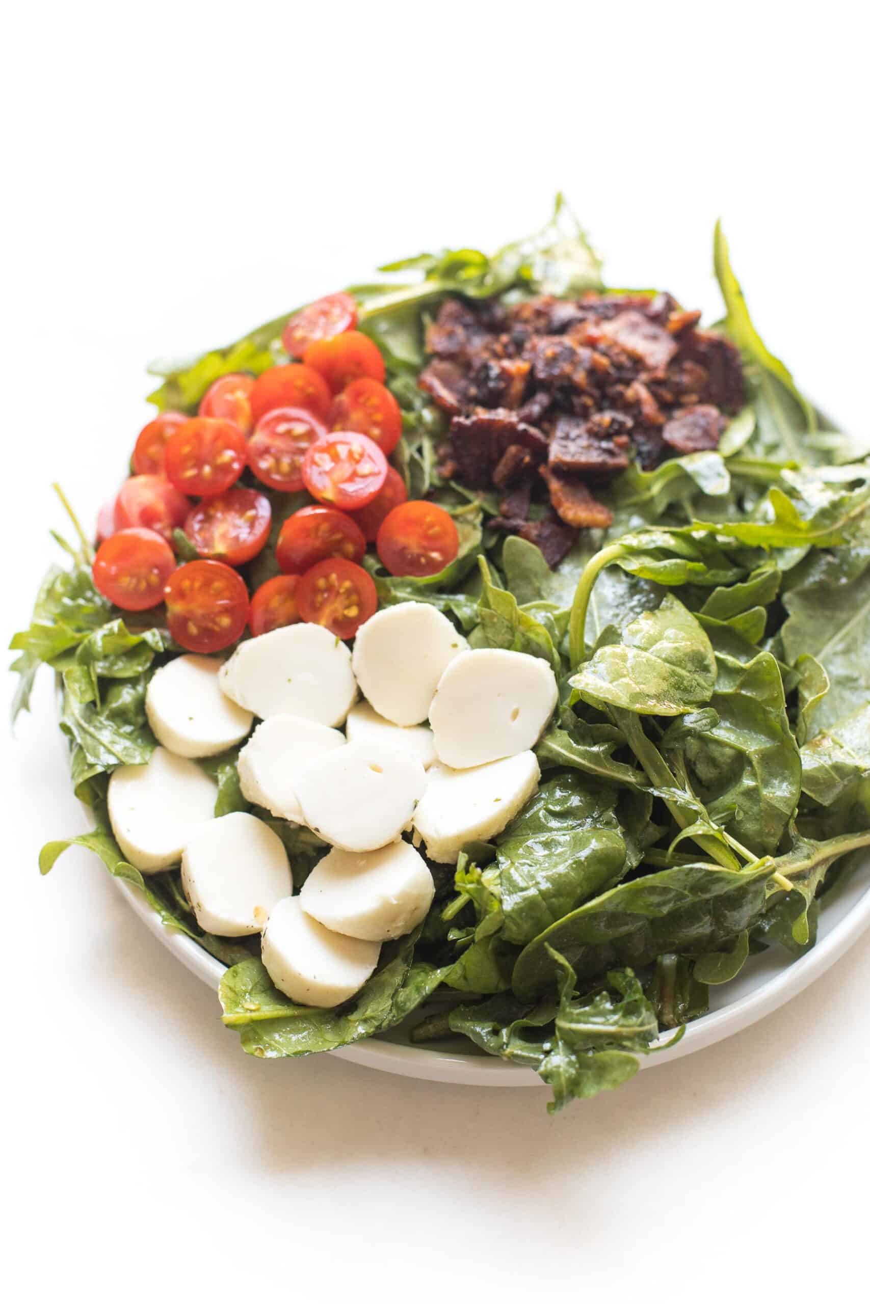 keto salad with bacon, tomatoes and mozzarella cheese on spinach and arugula on a white plate