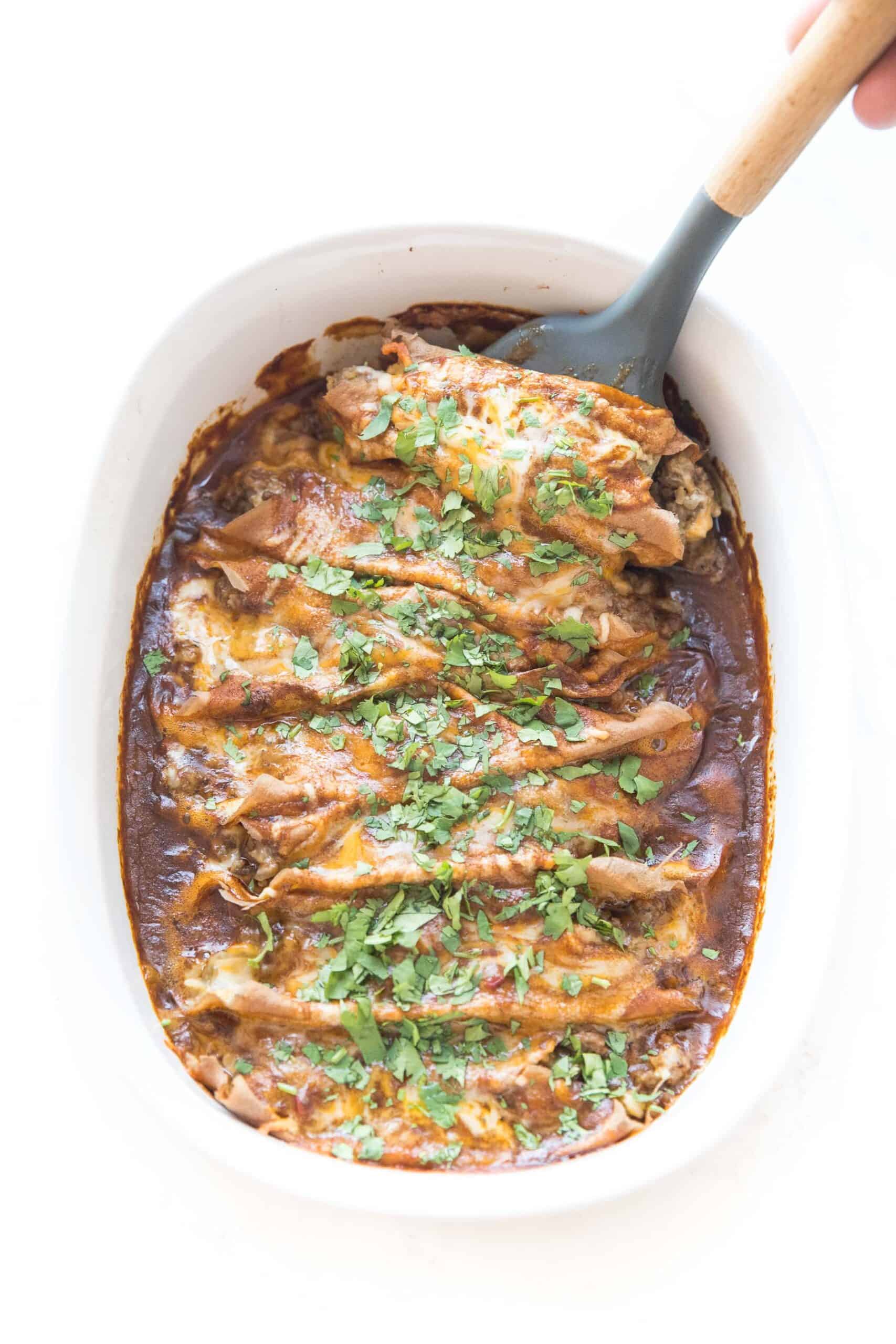 spatula scooping into keto beef enchiladas in a baking dish