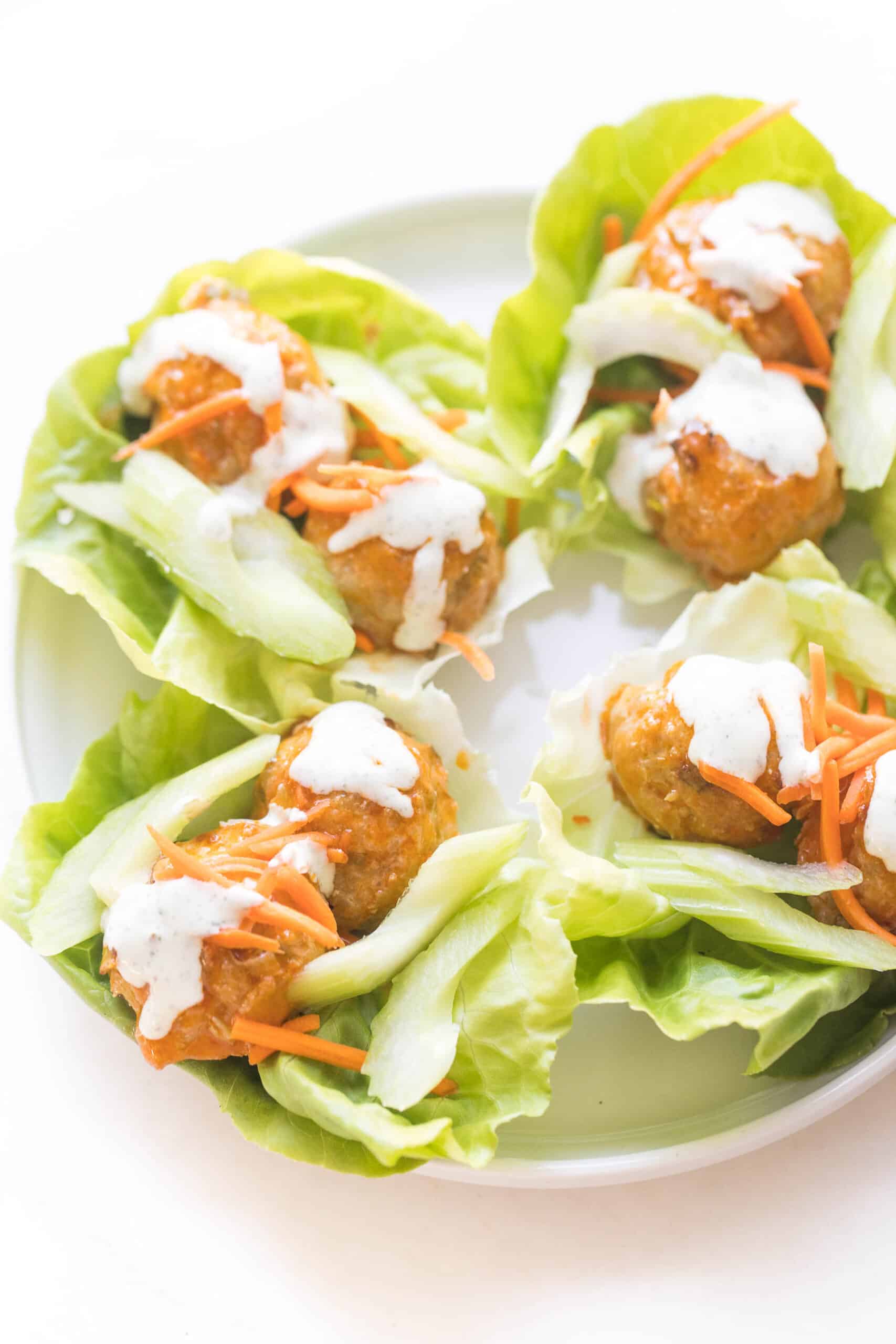 keto buffalo turkey meatballs on lettuce wraps topped with ranch dressing on a white plate and background