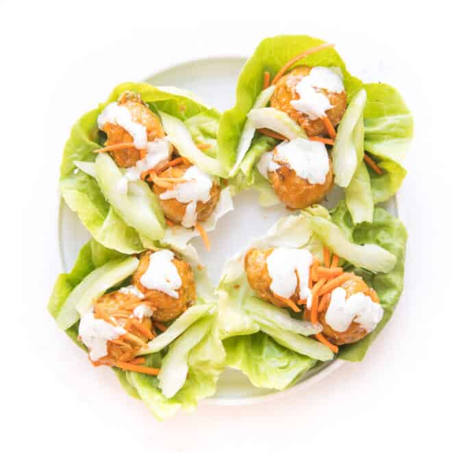 keto buffalo turkey meatballs on lettuce wraps topped with ranch dressing on a white plate and background