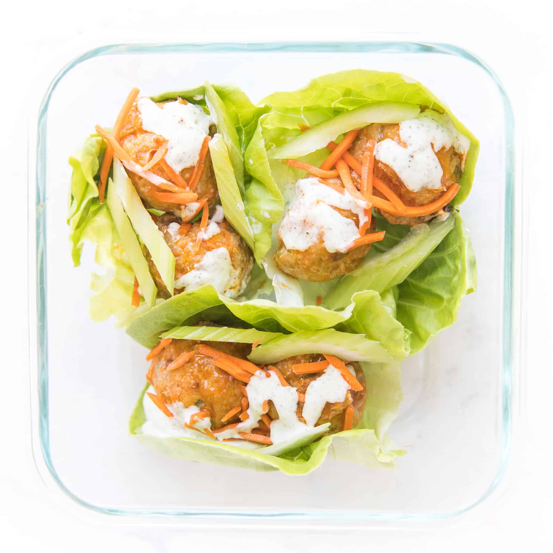 keto buffalo turkey meatballs on lettuce wraps topped with ranch dressing on a white plate and background