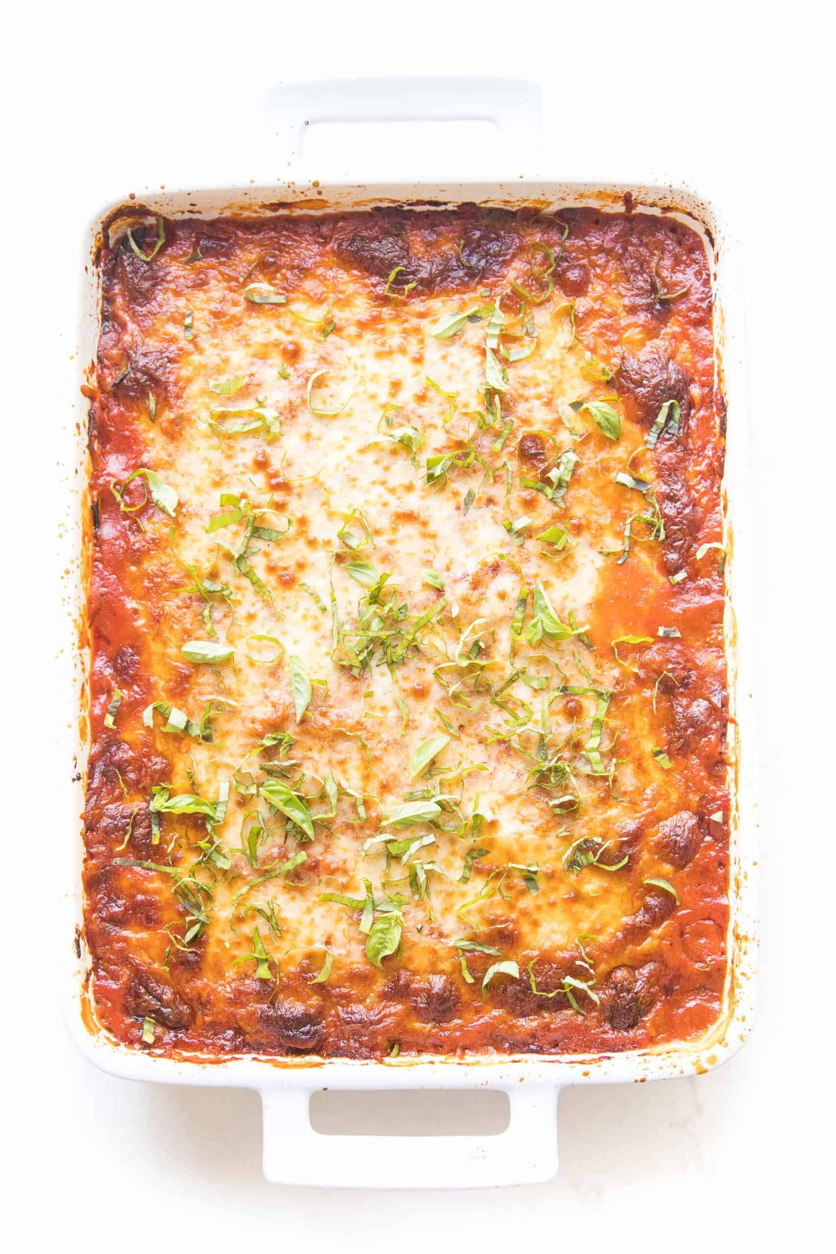 keto low carb lasagna made with zucchini noodles in a white baking dish topped with basil