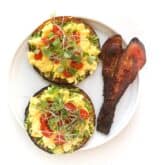 keto avocado toast topped with egg, tomatoes, microgreens and bacon on a white plate and background