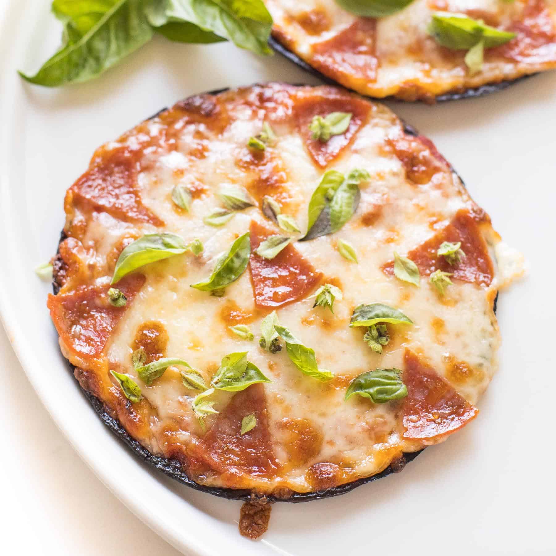 keto mini cauliflower thin pepperoni pizzas on a white plate topped with fresh basil