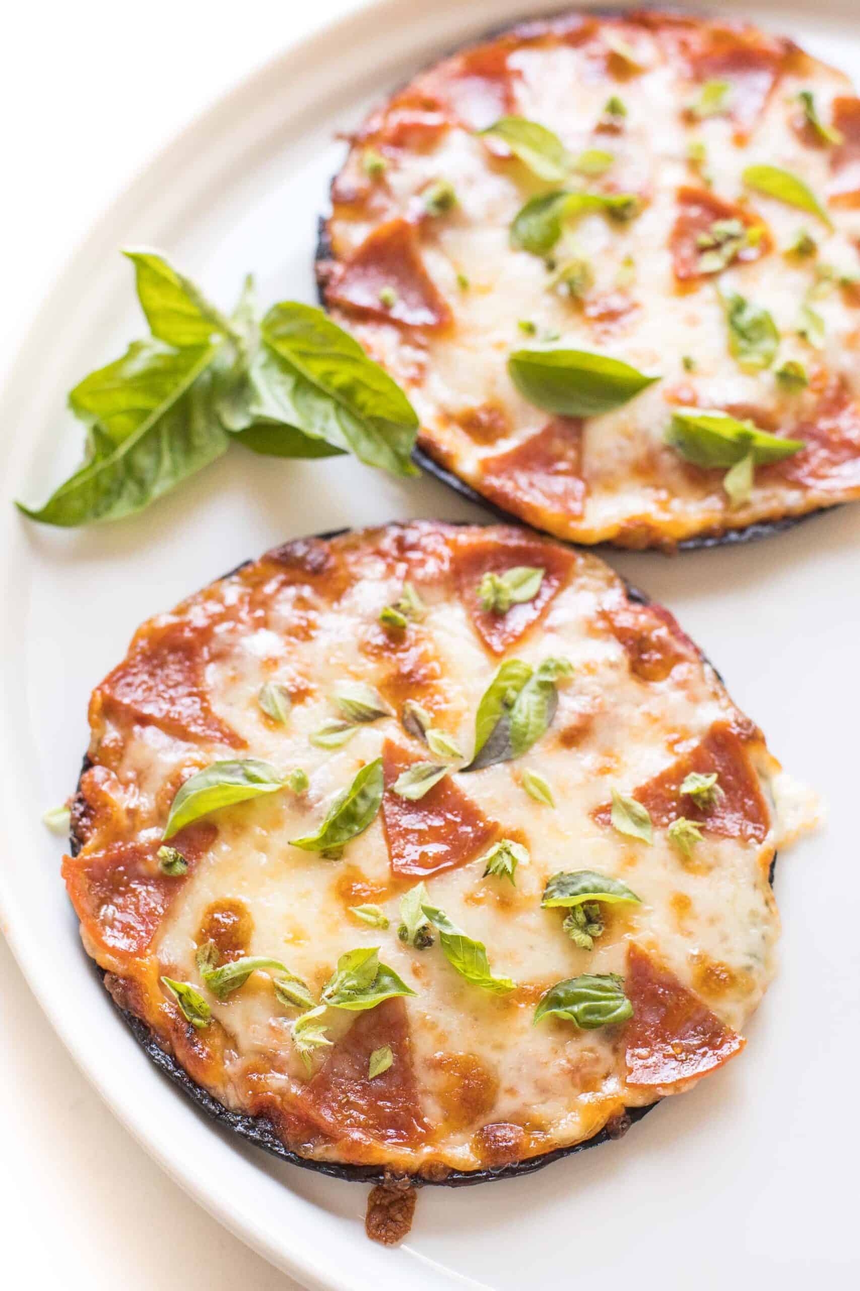 keto mini cauliflower thin pepperoni pizzas on a white plate topped with fresh basil