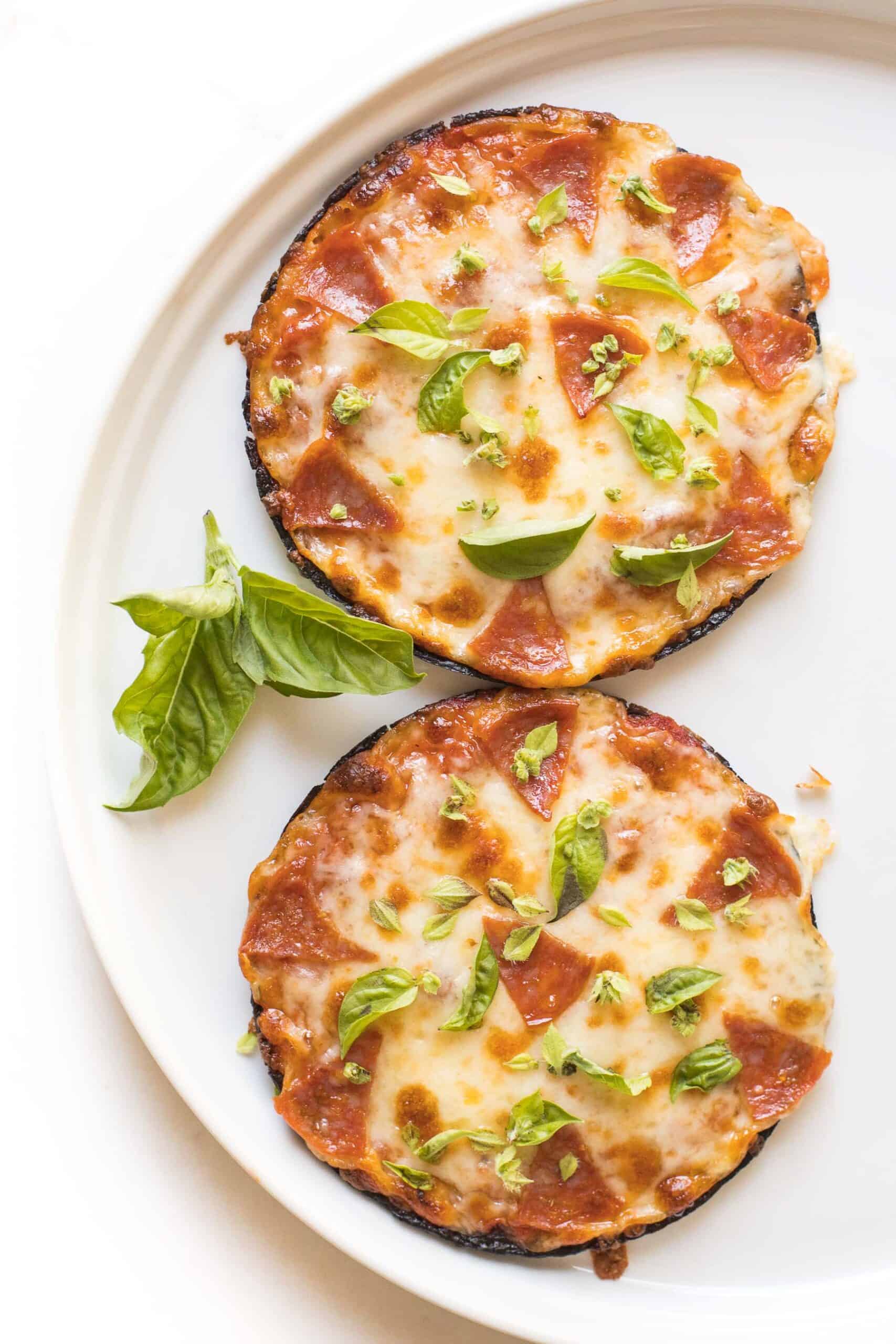 keto mini cauliflower thin pepperoni pizzas on a white plate topped with fresh basil