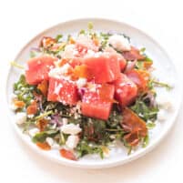 WATERMELON FETA SALAD WITH ARUGULA, CRISPY PROSCIUTTO AND RED ONION ON A WHITE PLATE