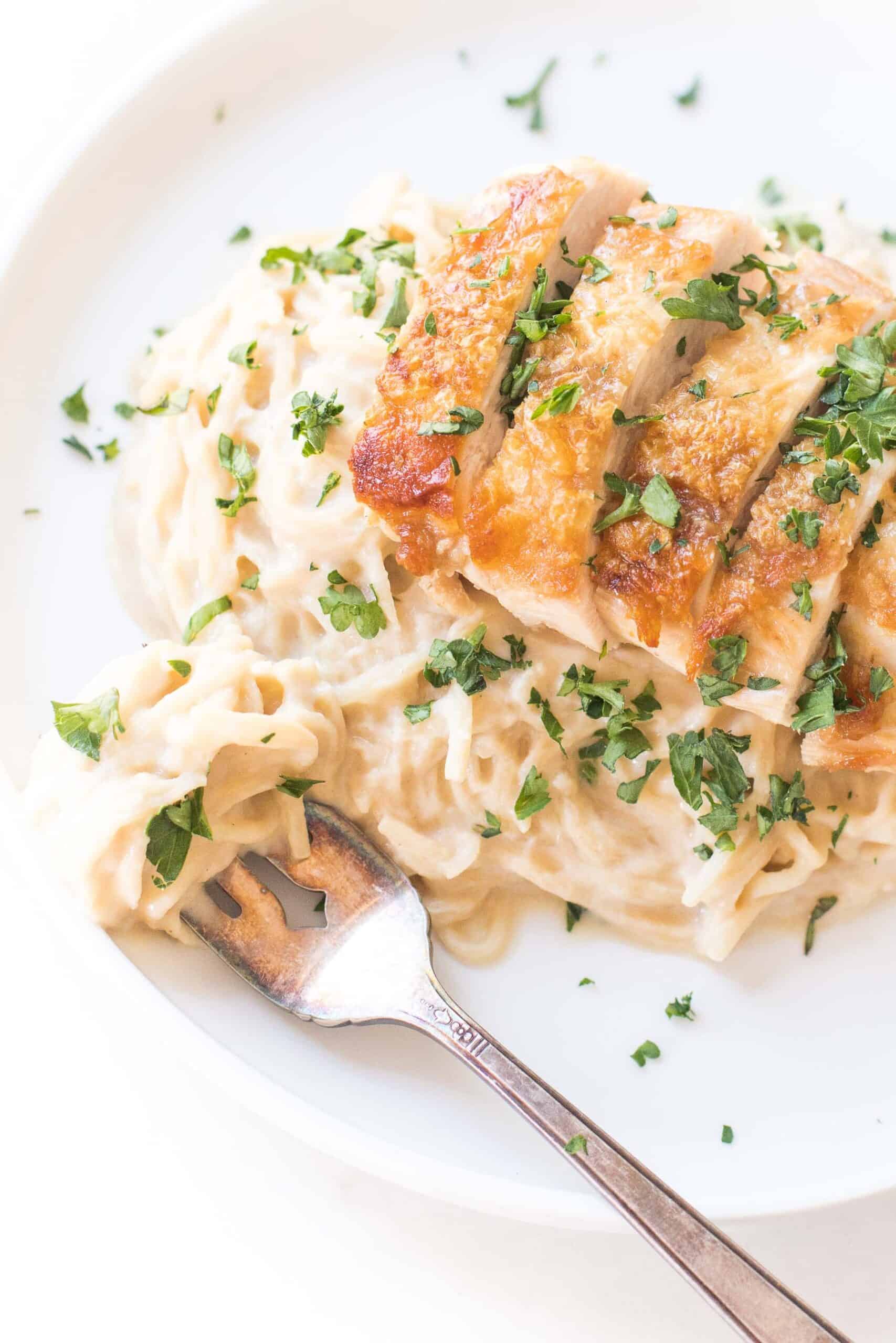 creamy chicken cauliflower alfredo pasta topped with fresh basil on a white plate