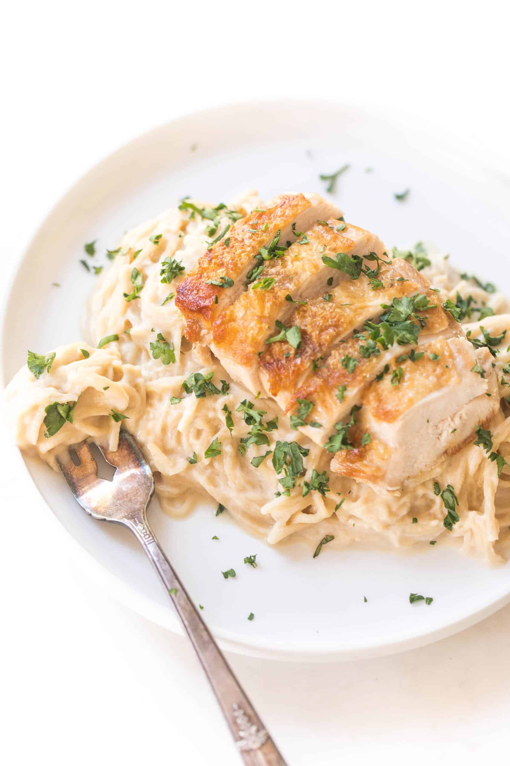 creamy chicken cauliflower alfredo pasta topped with fresh basil on a white plate