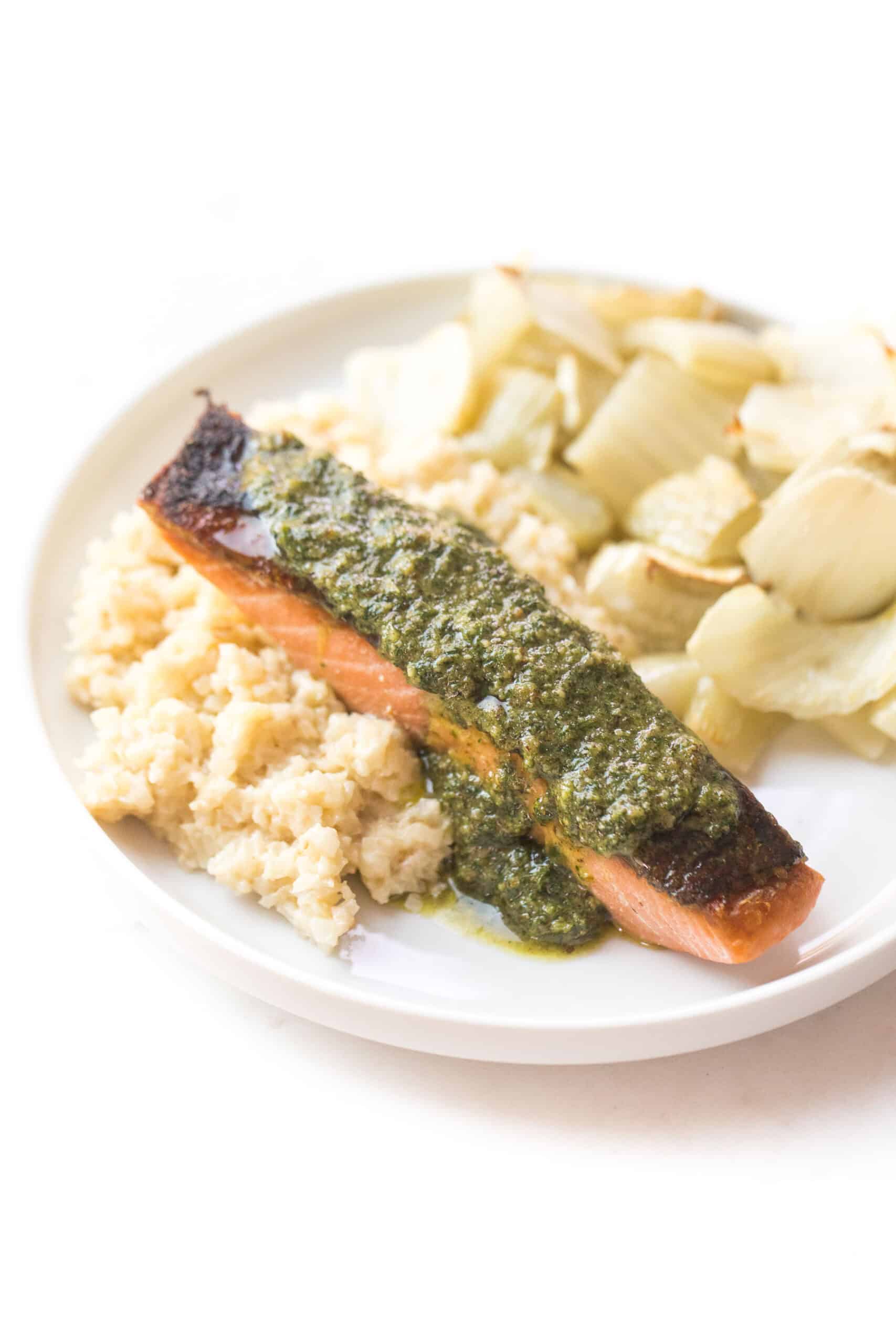 salmon topped with a green sauce on a white plate and background