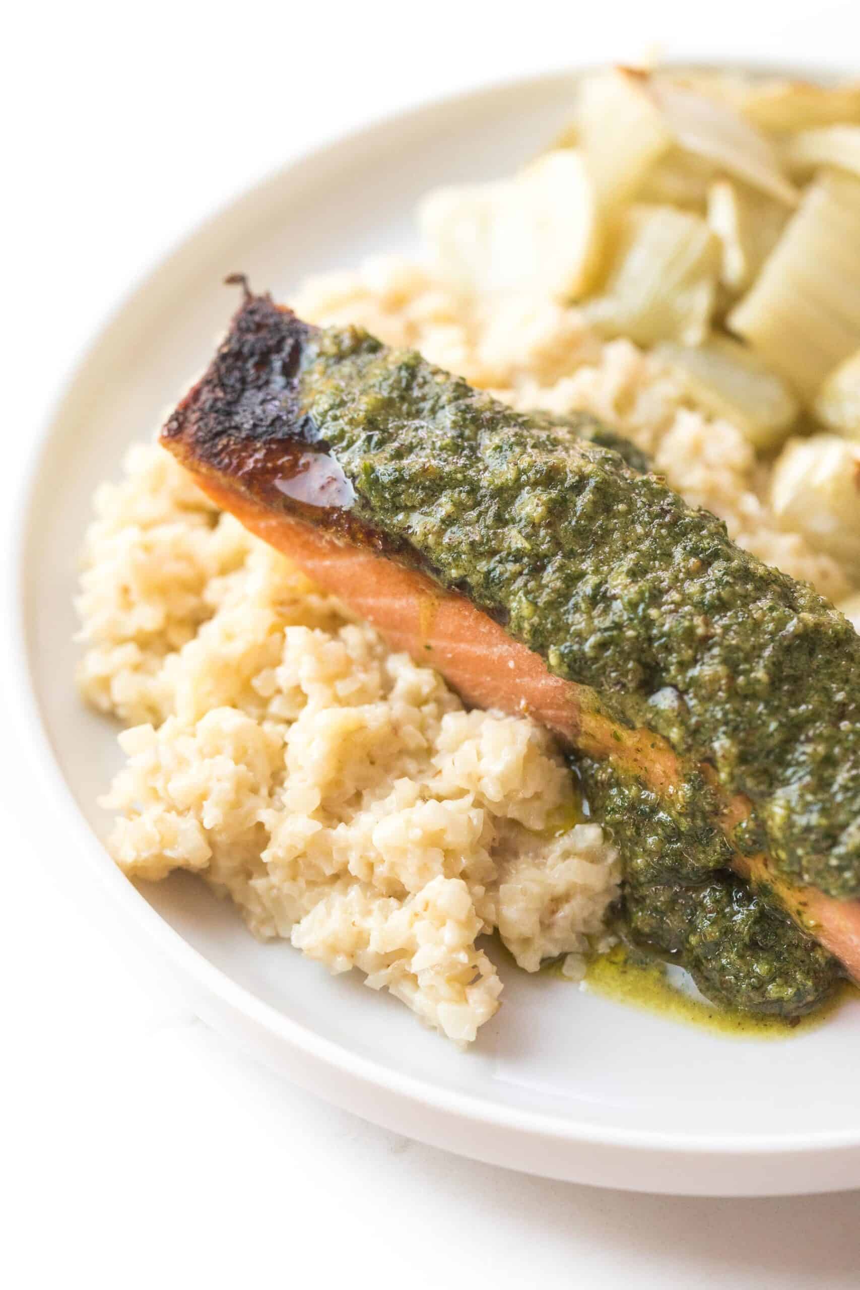 salmon topped with a green sauce on a white plate and background