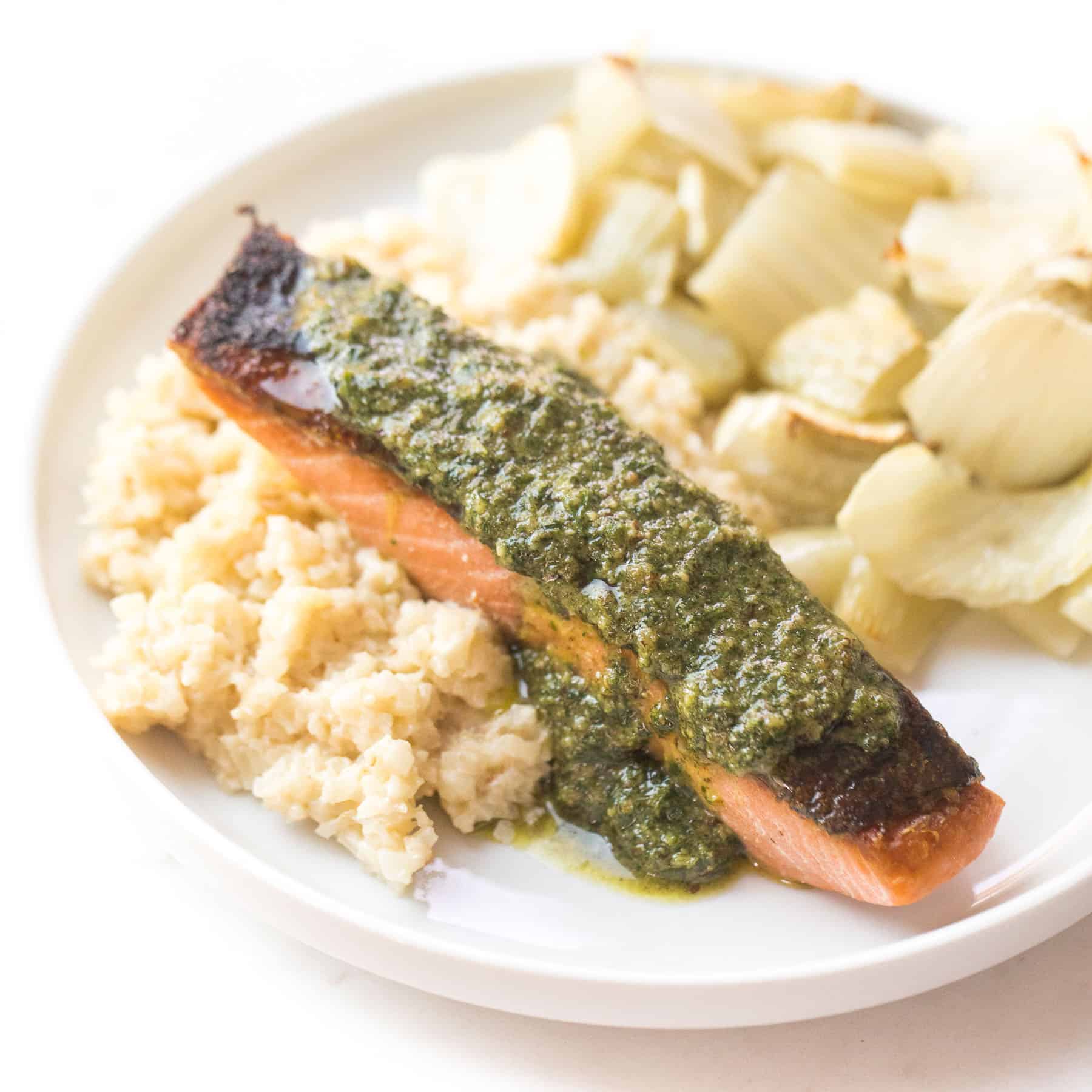 salmon with orange parsley sauce on a white plate with cauliflower rice