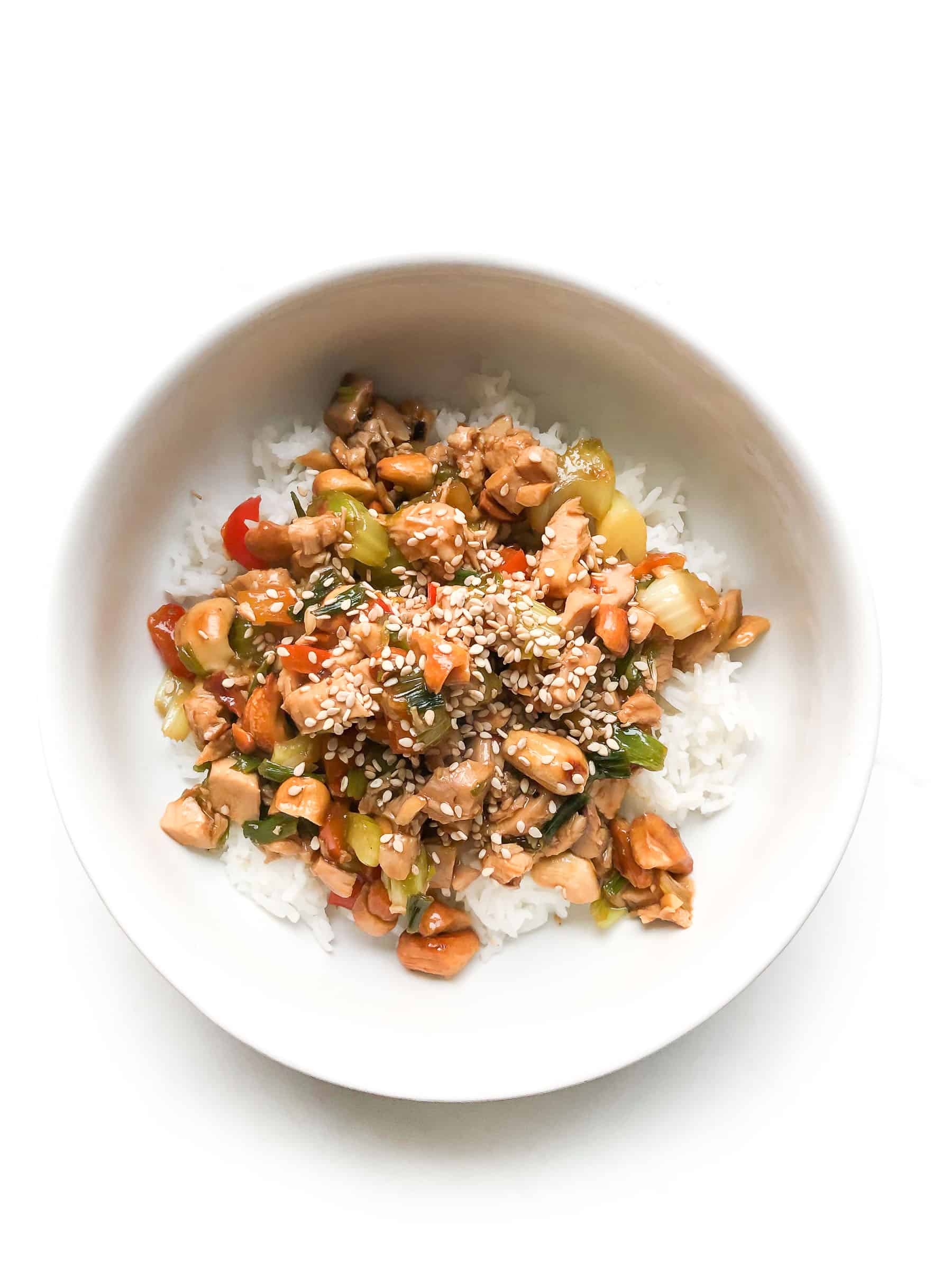 CHICKEN AND CELERY STIR FRY IN A WHITE BOWL TOPPED WITH SESAME SEEDS OVER CAULIFLOWER RICE