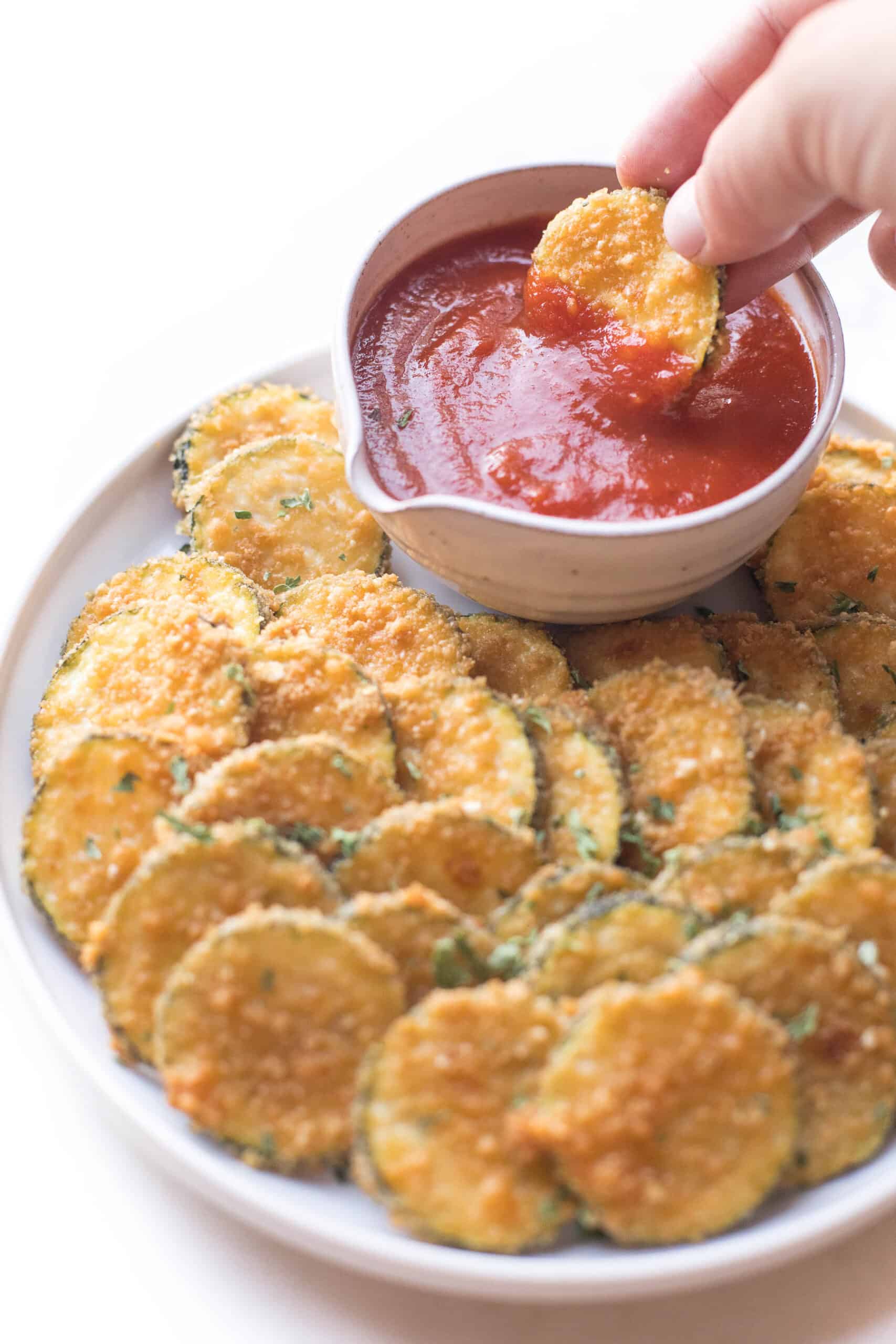 Crispy parmesan zucchini bites appetizer being dipped in marinara sauce