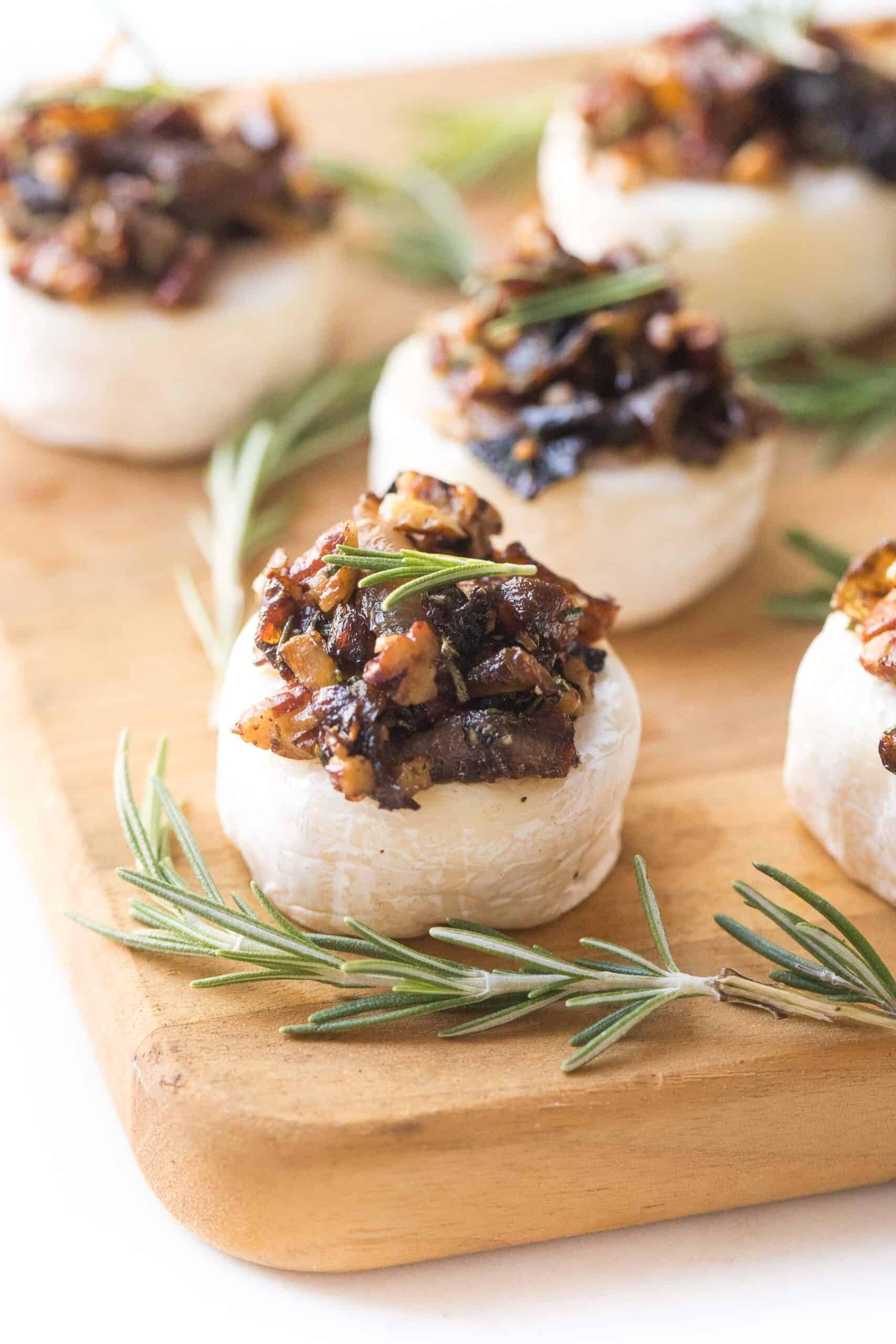 Brie cheese bites topped with caramelized onions, rosemary and pecan mixture on a cheese board