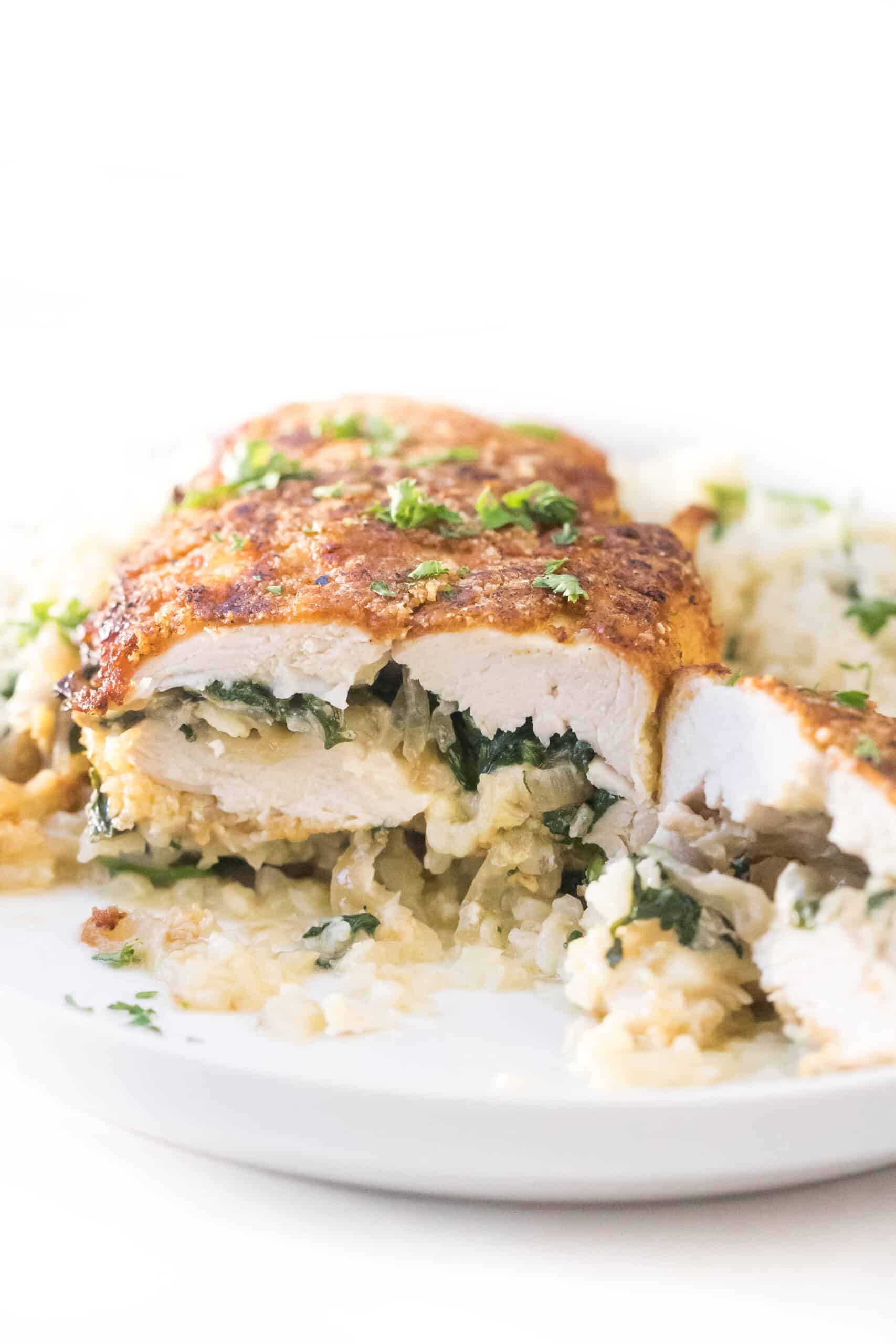 keto brie + spinach stuffed chicken breast cut in half on a white plate with cauliflower rice