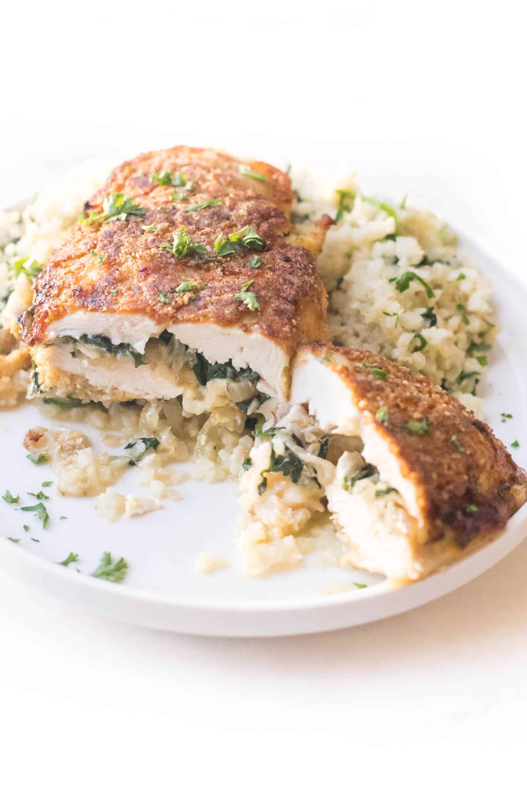 keto brie + spinach stuffed chicken breast cut in half on a white plate with cauliflower rice