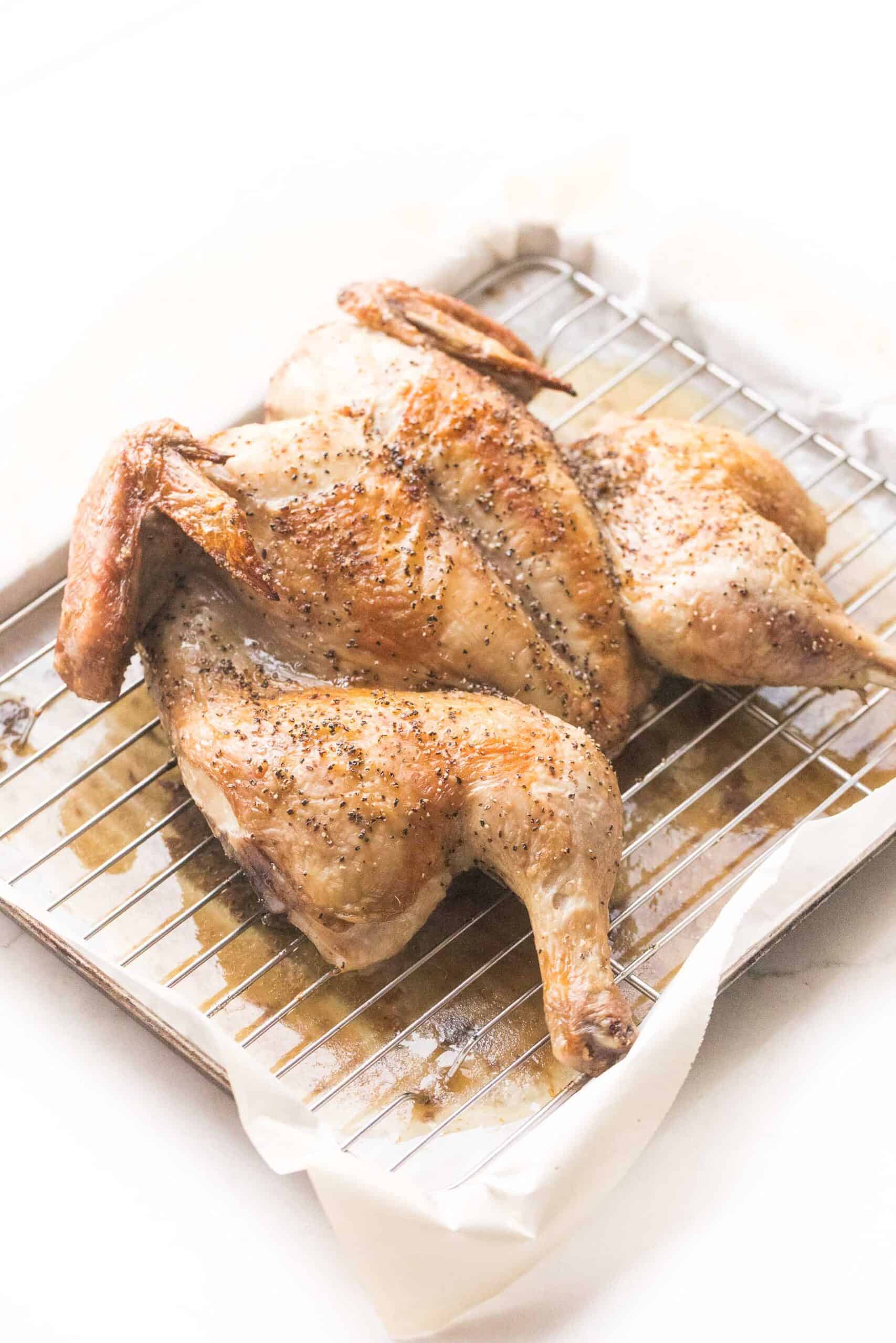 spatchcock roasted chicken with golden brown skin on a rimmed baking sheet