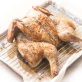 spatchcock roasted chicken with golden brown skin on a rimmed baking sheet