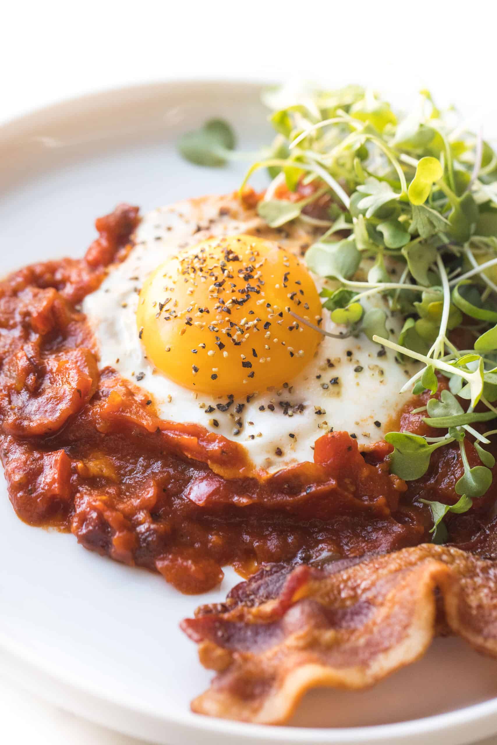 KETO SHAKSHUKA EGGS IN TOMATO SAUCE ON A WHITE PLATE ON A WHITE BACKGROUND