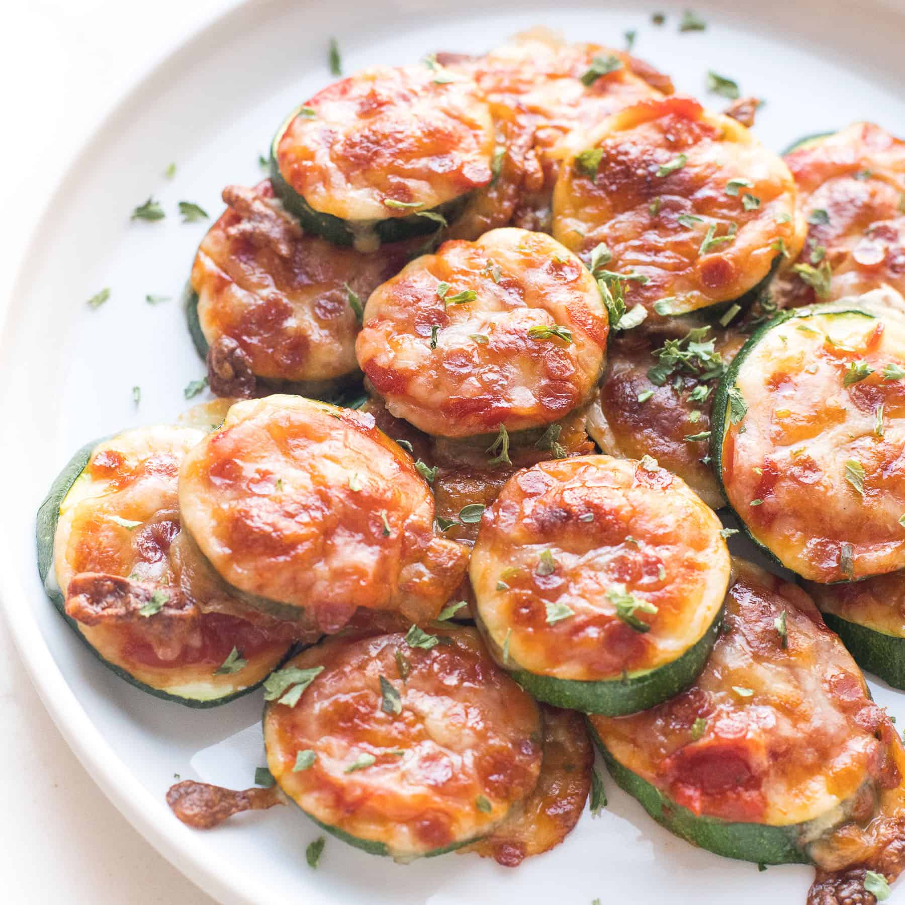 keto mini zucchini pizza bites on a white plate and background