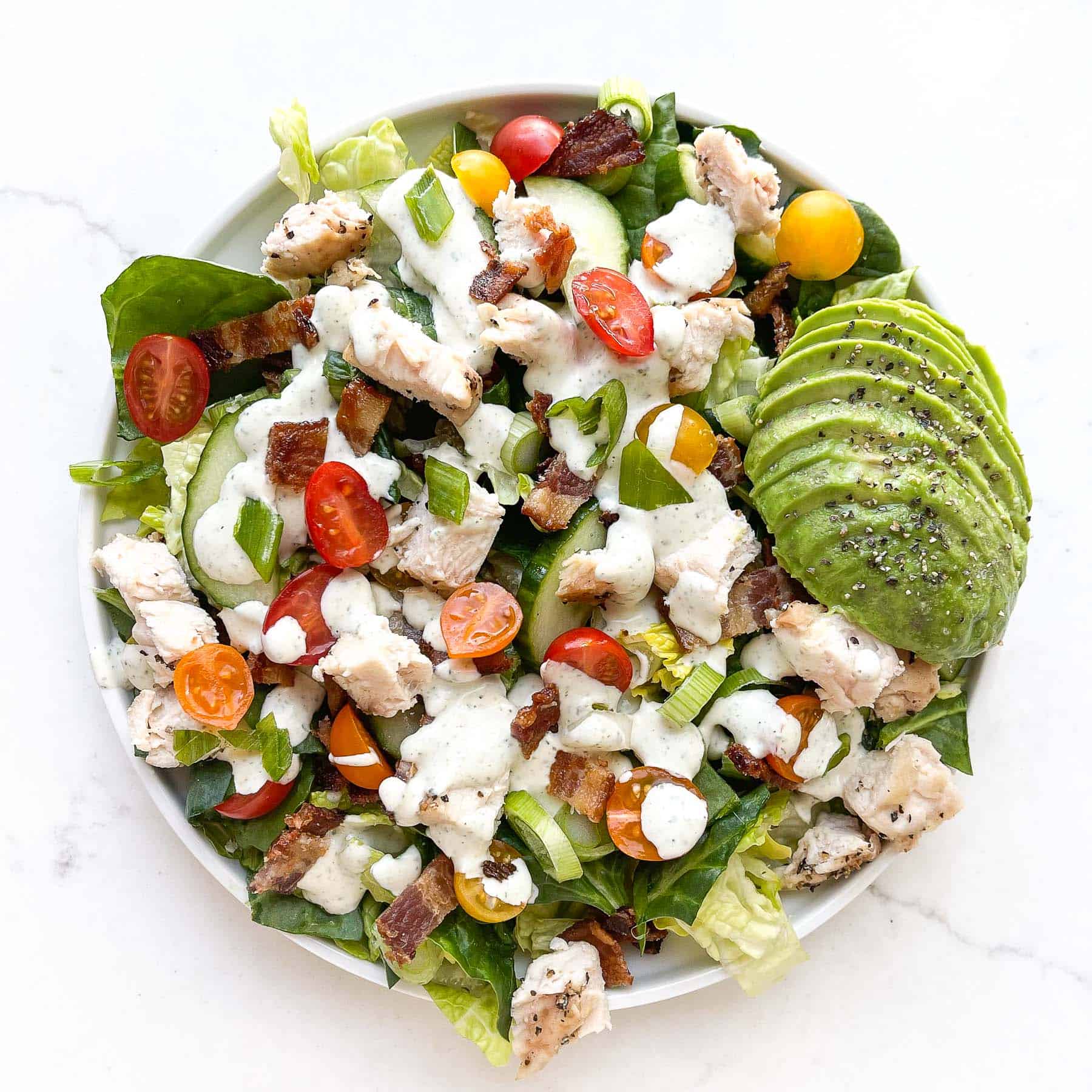 Salad topped with ranch dressing, chicken, avocado, tomatoes, bacon.