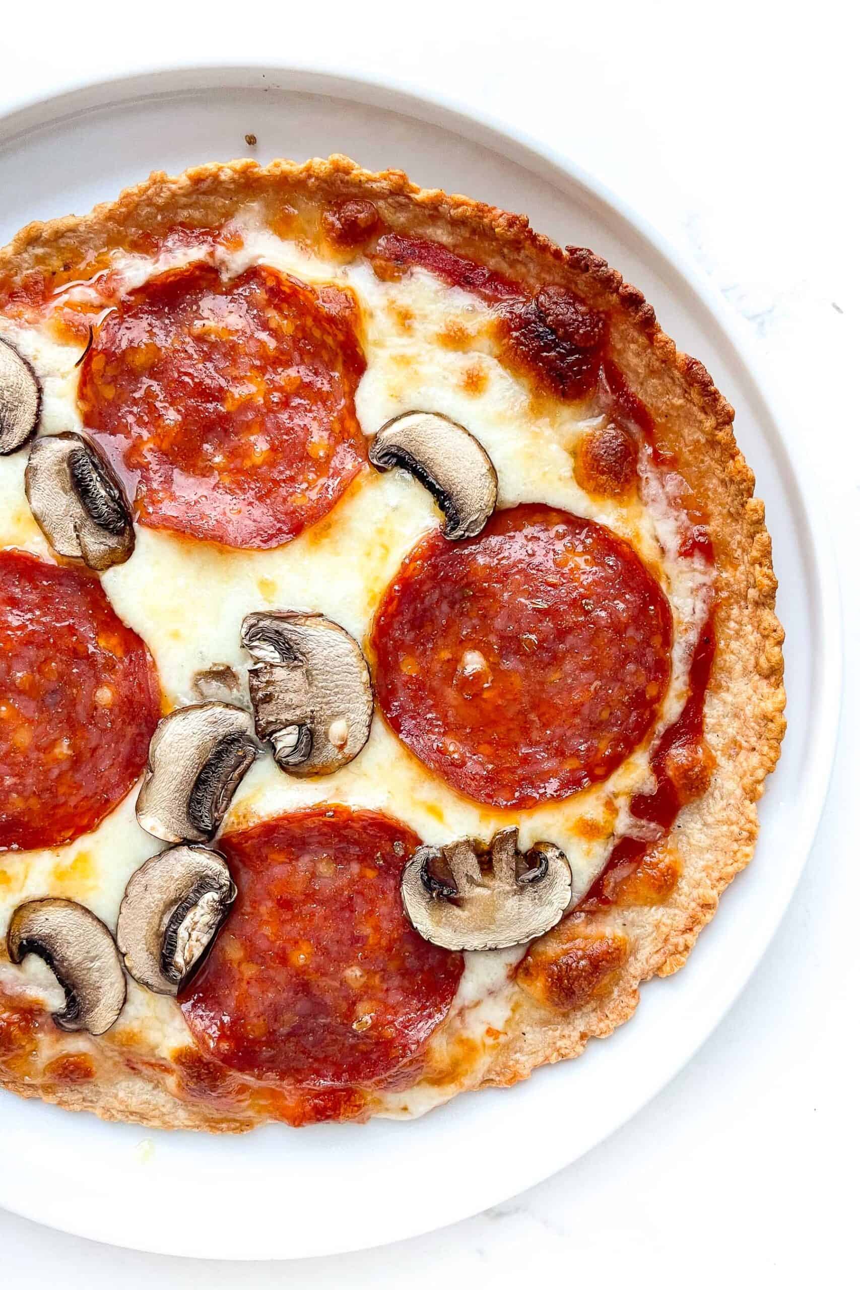 zero carb pepperoni and mushroom pizza on a white plate and background