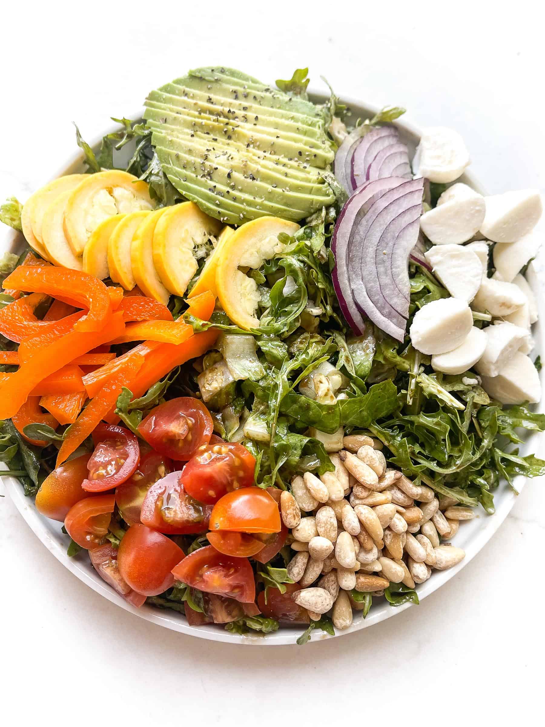 rainbow chopped salad with tomatoes, bell pepper, squash, avocado, red onion, mozzarella + pinenuts over arugula