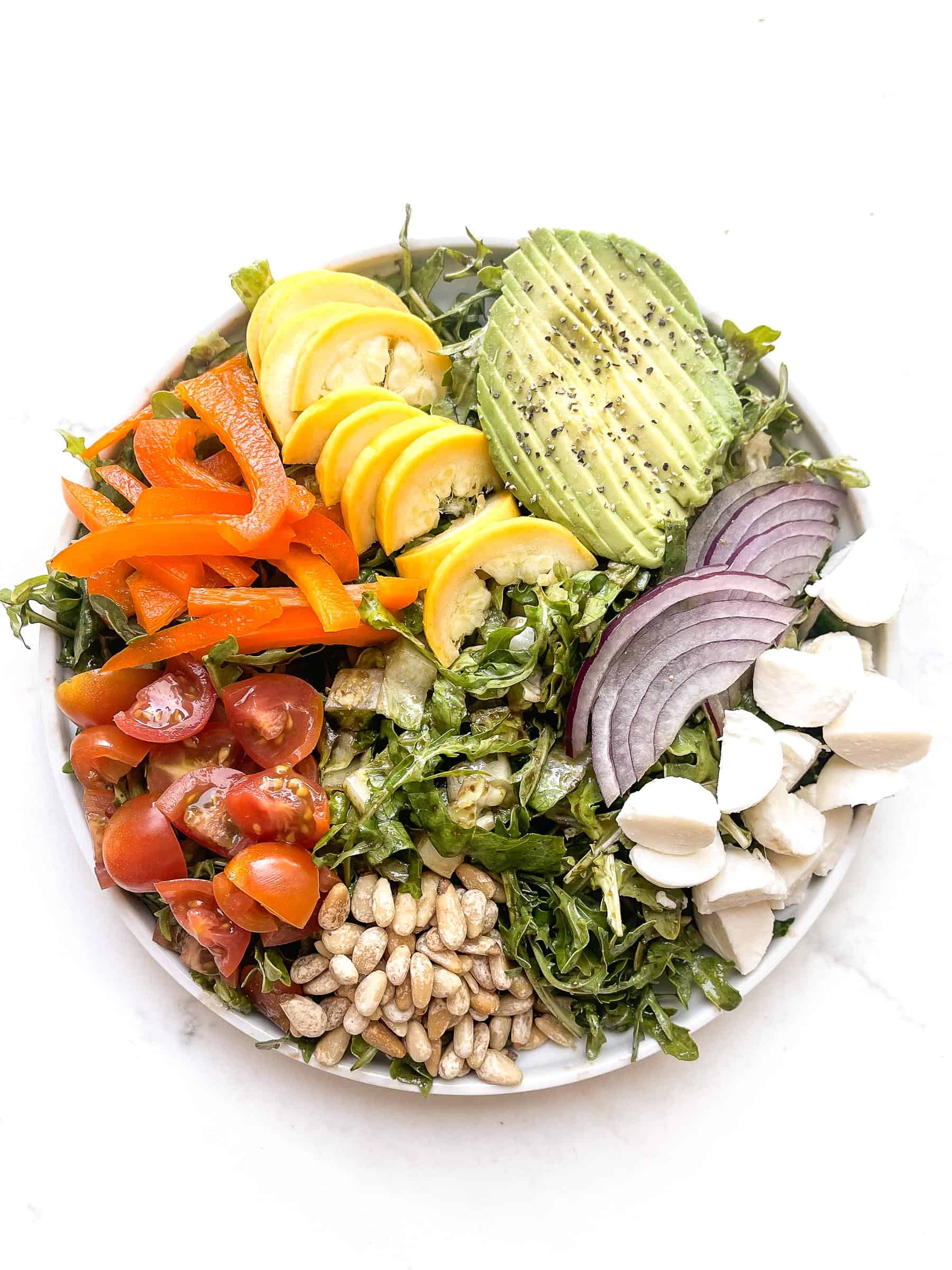 rainbow chopped salad with tomatoes, bell pepper, squash, avocado, red onion, mozzarella + pinenuts over arugula