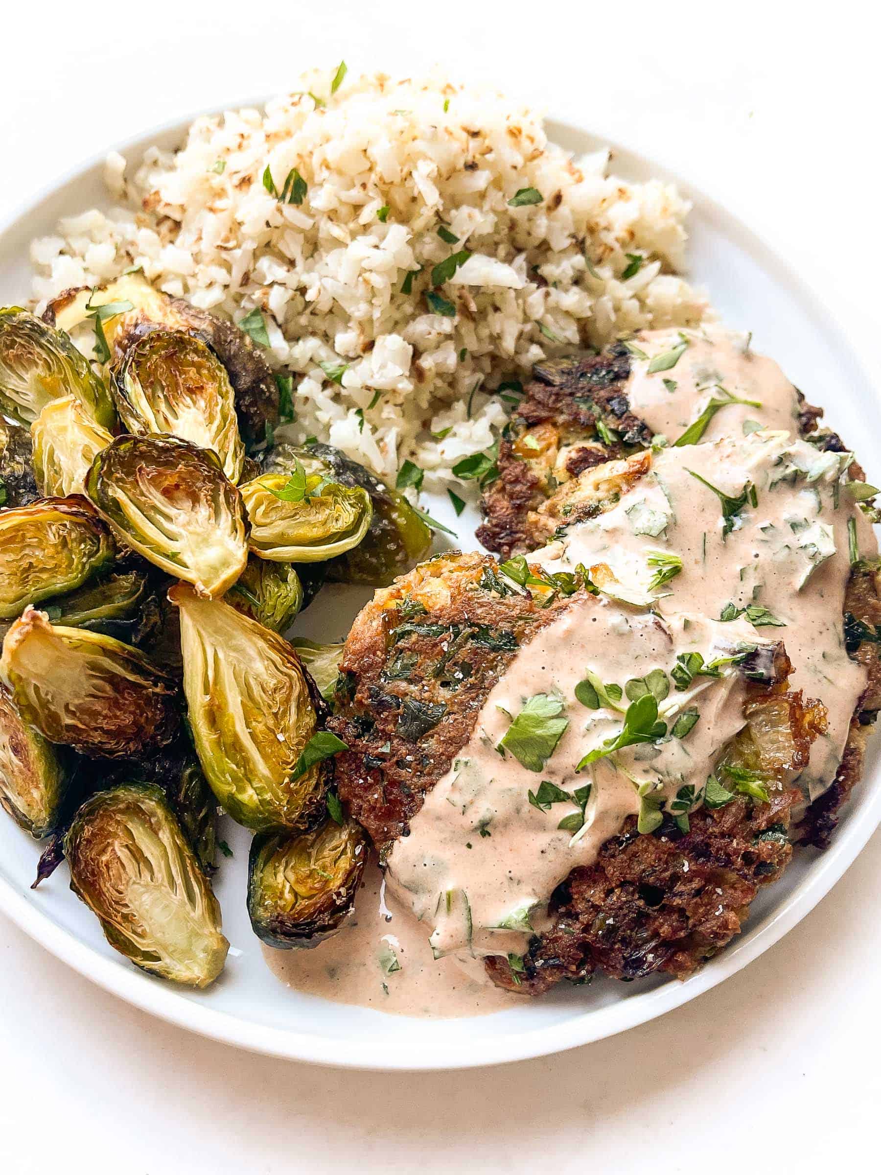 keto southwest tuna cakes topped with sauce on a white plate and background with roasted brussels sprouts and cauliflower rice