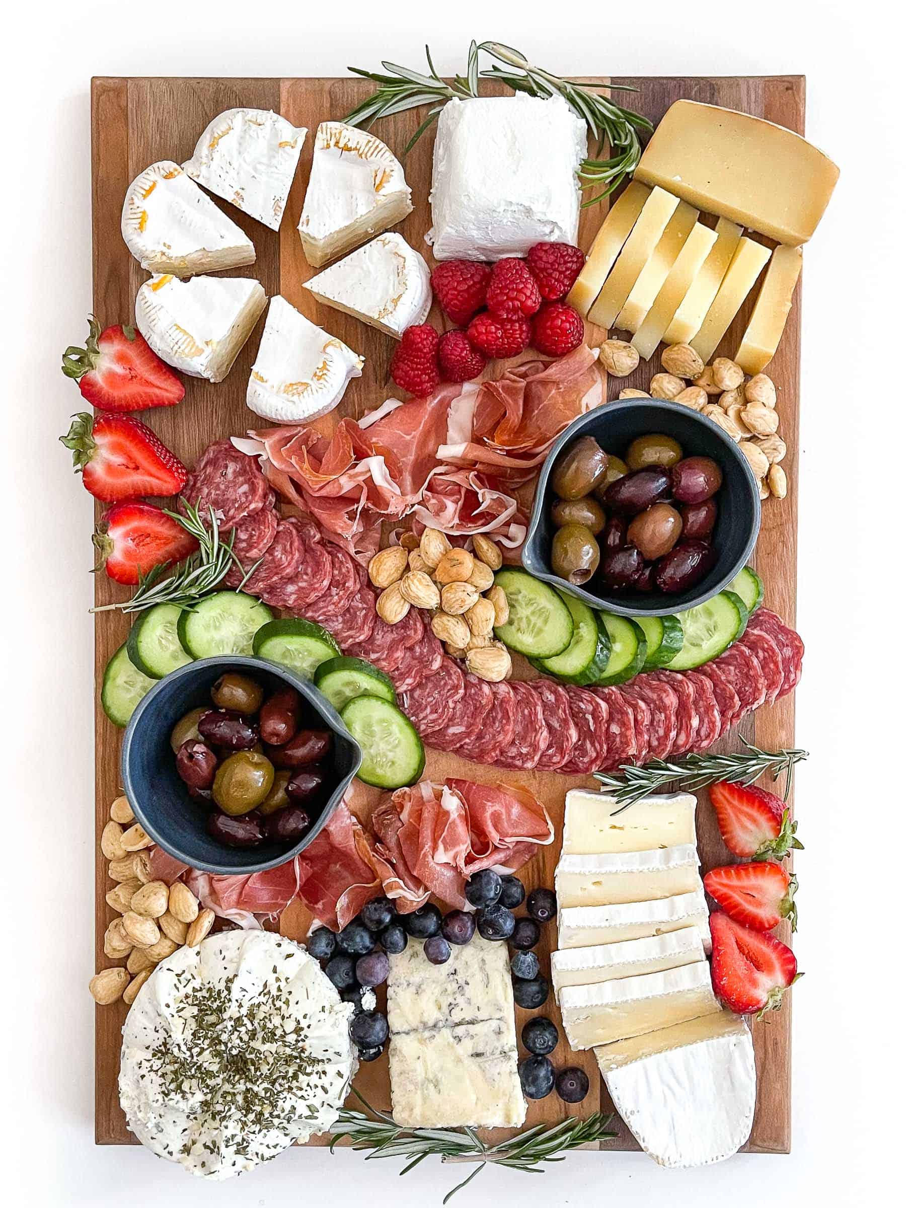 Keto friendly cheese board with sliced cheese, salami, cucumber, nuts, olives and berries