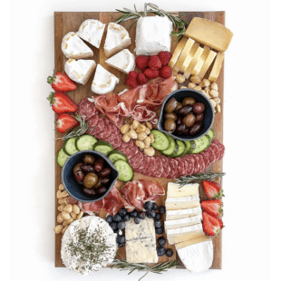 Keto friendly cheese board with sliced cheese, salami, cucumber, nuts, olives and berries