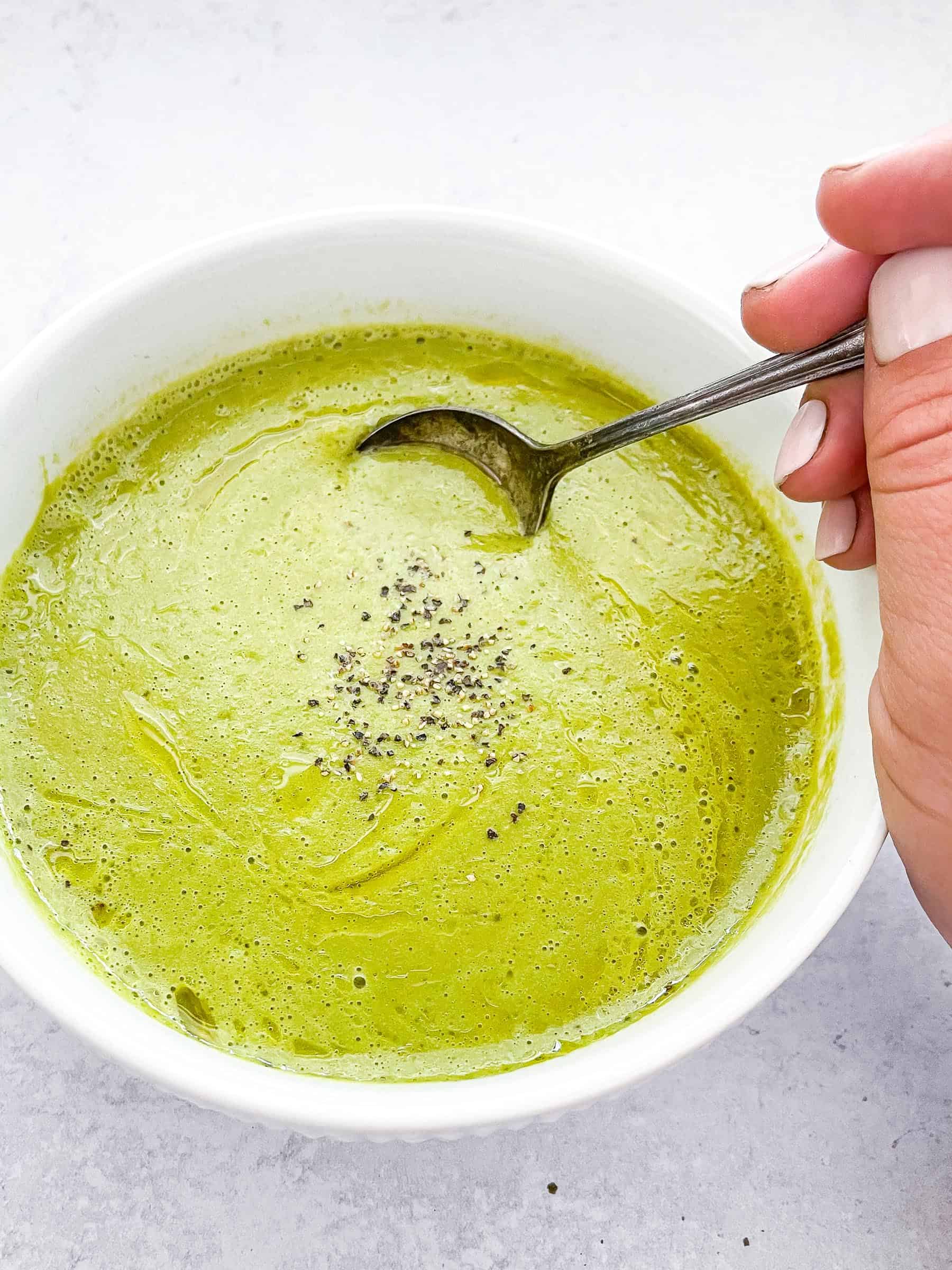 hand holding a spoon in green cream of asparagus soup on a white background