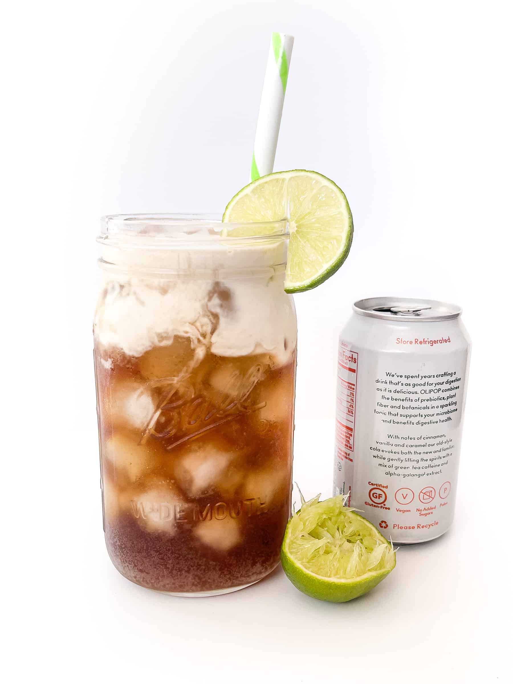dirty soda in a glass mason jar with a lime wedge and a straw next to a can of soda and a sqeezed lime