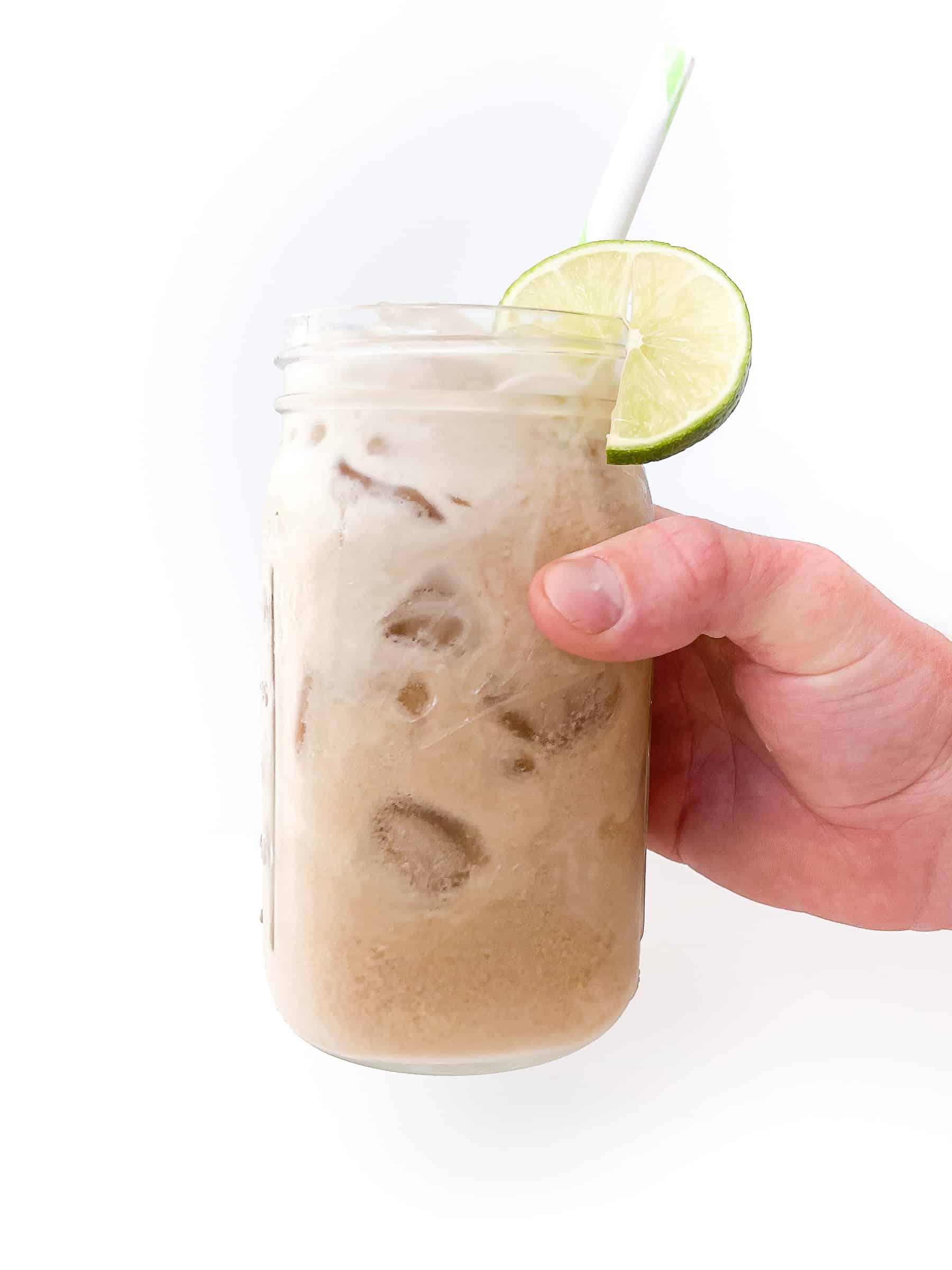 a hand holding a glass mason jar will fill dirty diet coke, lime, and creamer with a lime to garnish and a straw