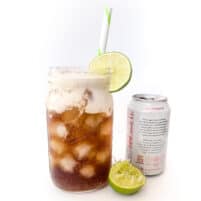 mason jar full of soda topped with cream with a straw and lime garnish on a white background
