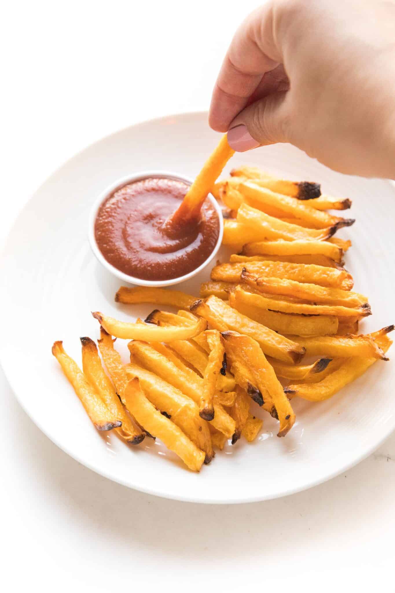a hand dipping keto french fries dipping in keto ketchup on a white plate