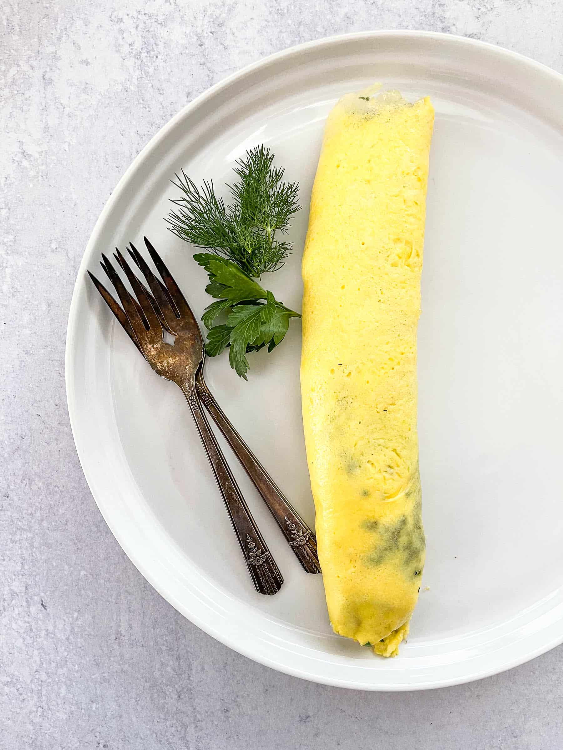 french omelet on white plate garnished with dill and parsley with two antique forks