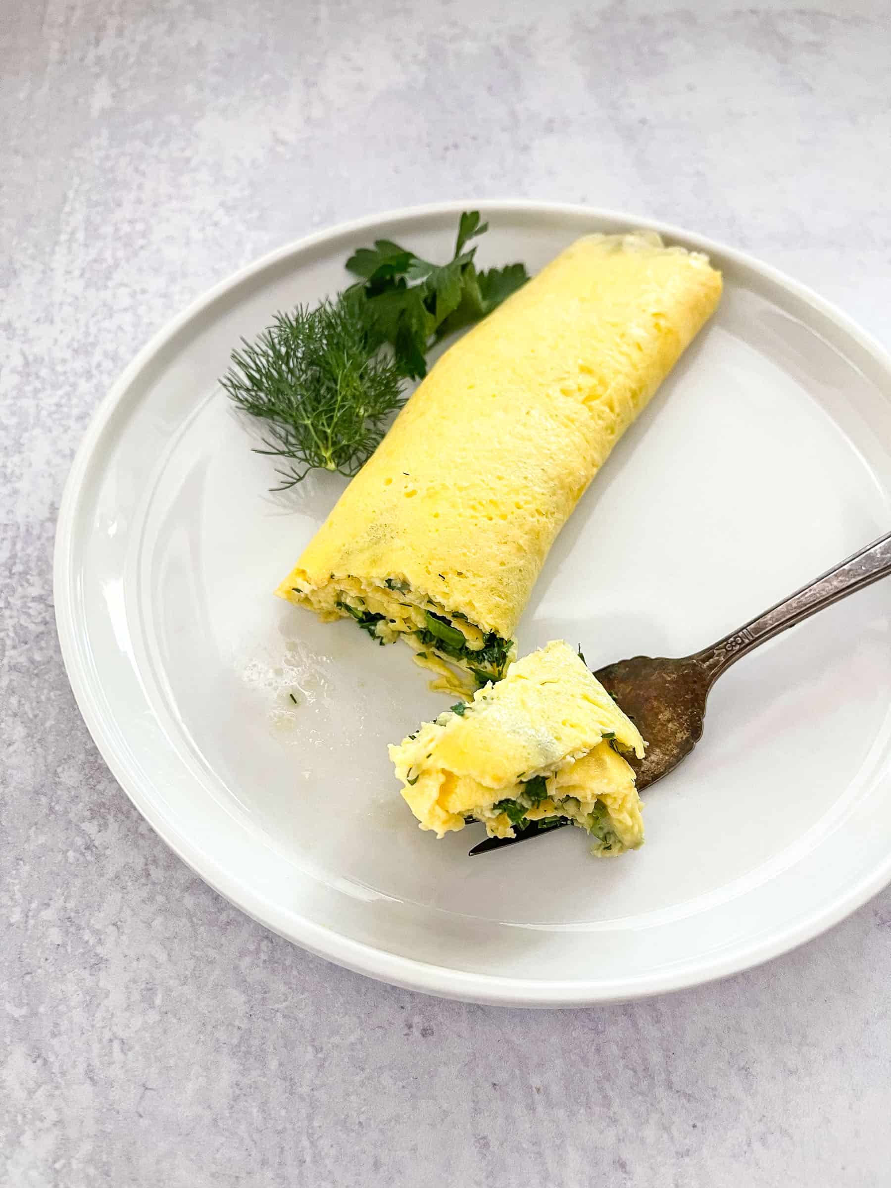 french omelet on white plate garnished with dill and parsley with antique fork