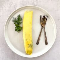 french omelet on white plate garnished with dill and parsley with two antique forks