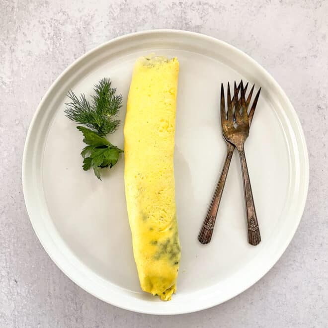 french omelet on white plate garnished with dill and parsley with two antique forks