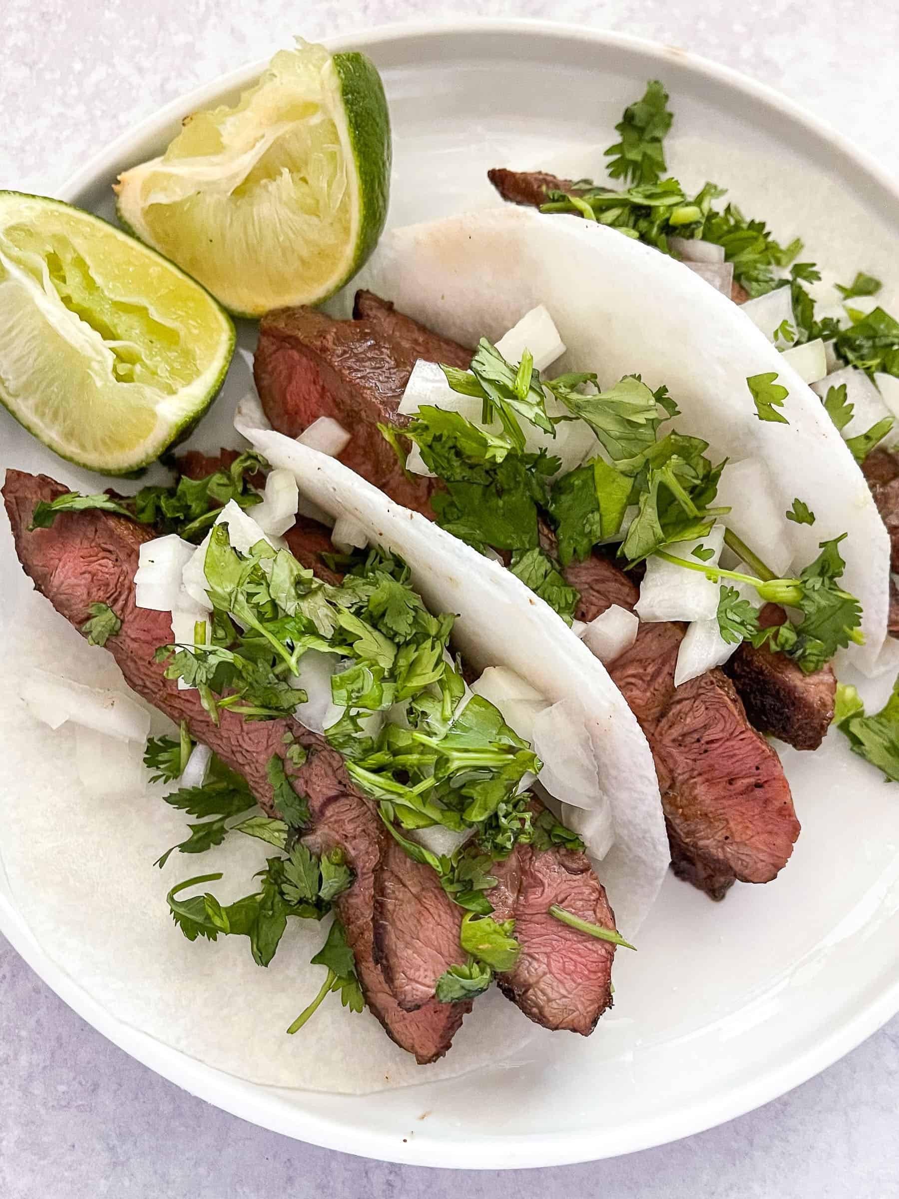 steak tacos on jicama wrap on a white plate with lime and a white background