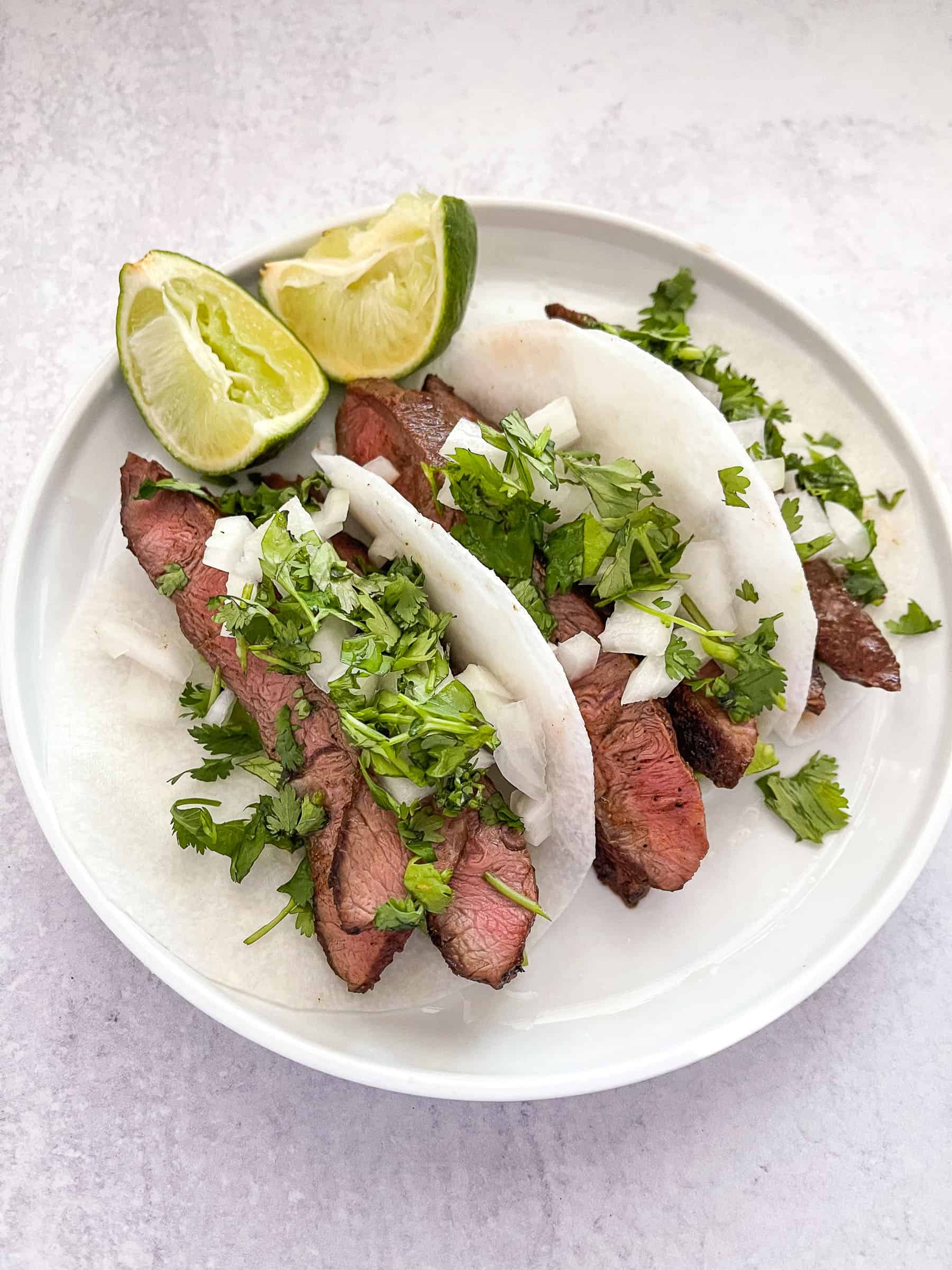steak tacos on jicama wrap on a white plate with lime and a white background