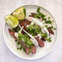 steak tacos on jicama wrap on a white plate with lime and a white background